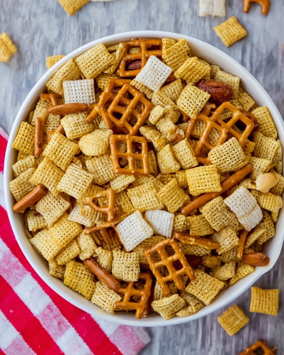A close-up top view of a white bowl filled with a mix of snack pieces. The base layer is made of small square yellow crunchy cereal pieces with a grid texture, scattered evenly. Mixed among this are flat, white rectangular chips, distributed throughout the bowl. On top of these, there are square pretzels with a lattice pattern and a light brown, slightly shiny surface sprinkled with coarse salt. Thin, curved light brown snack sticks and small tan-colored nuts are sprinkled intermittently among the other pieces. The bowl sits on a white marbled surface, with the edge of a red-and-white striped napkin visible at the bottom edge. The image is well-lit, showing the textures and colors clearly. photo taken with an iphone --ar 4:5 --v 7