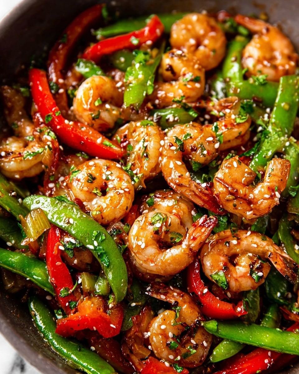 This close-up image shows a vibrant shrimp stir-fry with shrimp as the main focus, cooked to a light golden brown color with slight char marks, mixed with bright green snap peas and long, thin red bell pepper slices. The dish is sprinkled with white sesame seeds and finely chopped green herbs, giving it a fresh look. The shrimp and vegetables are glossy with a light sauce, making them appear juicy and well-coated. The background is a white marbled surface, contrasting with the colorful food. Photo taken with an iphone --ar 4:5 --v 7