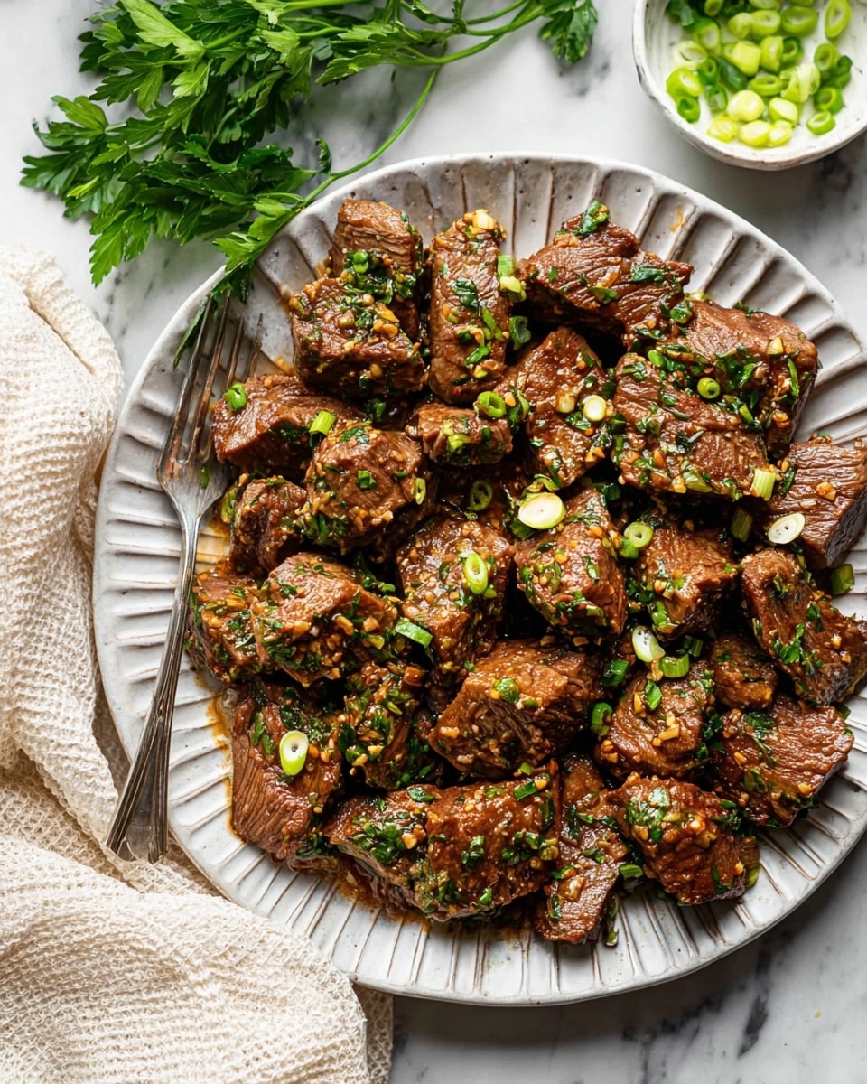 The image shows a single layer of cooked beef chunks on a round white plate with deep ridges along the edges. The beef pieces are brown and glazed with a shiny garlic and herb sauce, scattered with chopped green herbs and slices of green onions. A silver fork rests on the left side of the plate, partially tucked under some beef pieces. Fresh green parsley leaves are placed near the top left corner, and a small white bowl with more sliced green onions is visible in the upper right corner. The plate is set on a white marbled surface with a cream-colored textured cloth partially visible in the bottom left corner. Photo taken with an iphone --ar 4:5 --v 7