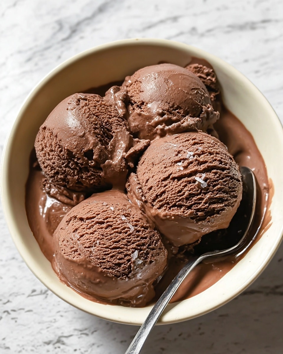 A close-up view of thick chocolate ice cream in a rectangular white tray, showing three long spreading marks made by a scoop or spatula, creating rough and smooth textures in rich brown shades; the light catches the creamy surface, highlighting its cold, dense, and slightly glossy appearance against a white marbled surface. photo taken with an iphone --ar 4:5 --v 7
