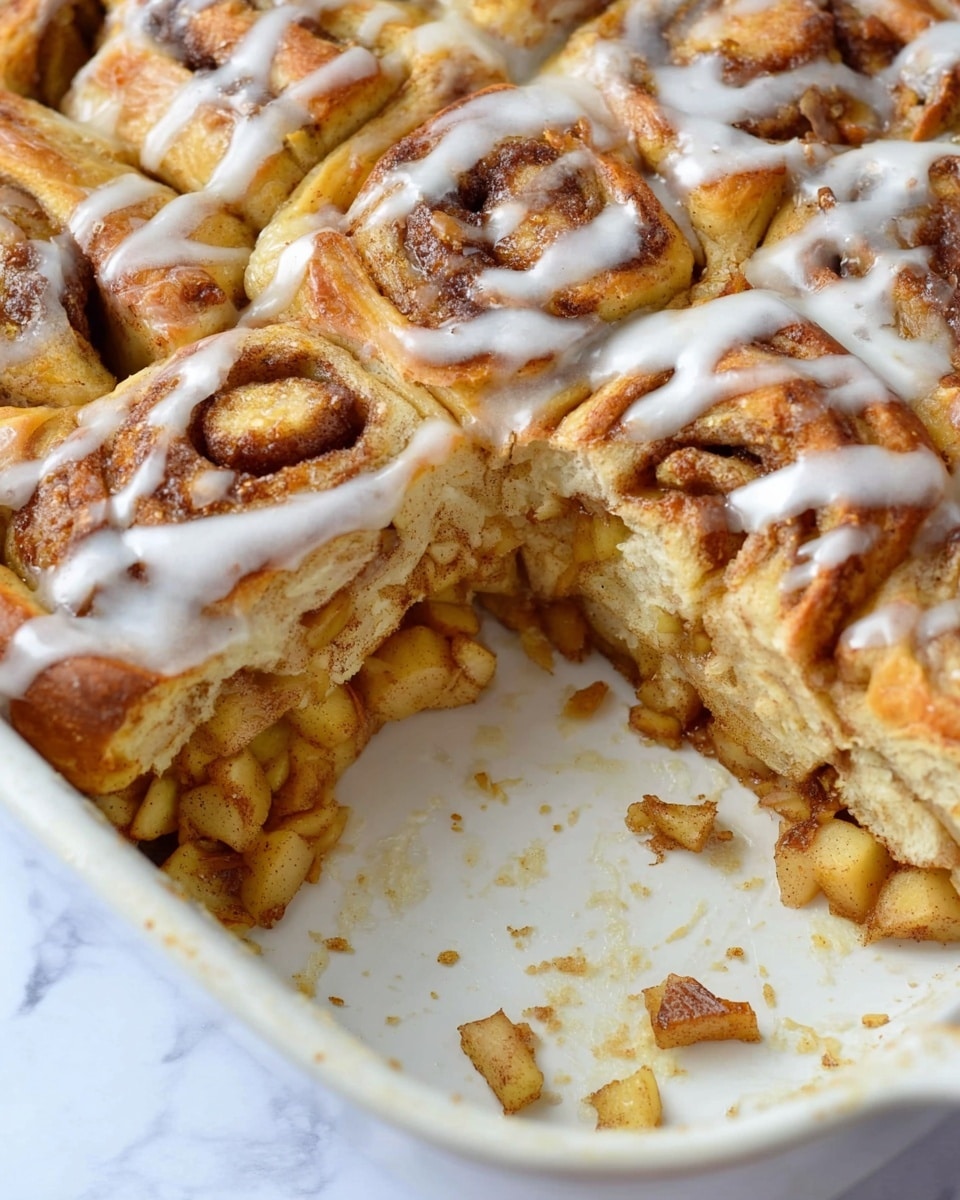 The image shows a close-up of a baked apple cinnamon pull-apart dish in a white baking dish with a section missing, exposing multiple layers inside. The top layer is golden-brown baked dough with swirls of cinnamon, covered in a thin white glaze that is drizzled unevenly. Underneath, there is a thick layer of cooked apple chunks mixed with cinnamon, showing a soft and glossy texture. The bottom layer is a baked crust that is slightly browned and firm, supporting the apple filling and dough above. Some apple pieces and crumbs are scattered in the empty space of the baking dish, all set against a white marbled surface. photo taken with an iphone --ar 4:5 --v 7