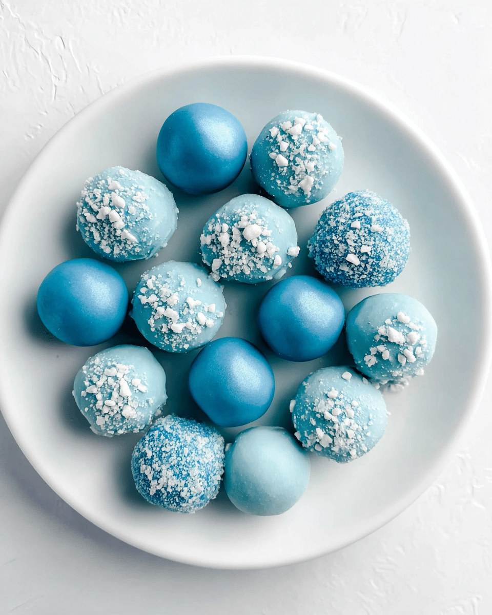 A white plate filled with 18 round truffles in two different styles, some smooth and shiny with a solid bright blue color, and others coated with a light blue powder and topped with white crunchy bits, creating a textured look. The truffles are randomly placed in a single layer, showing a mix of matte and glossy finishes against the clean white plate and white marbled texture background. photo taken with an iphone --ar 4:5 --v 7