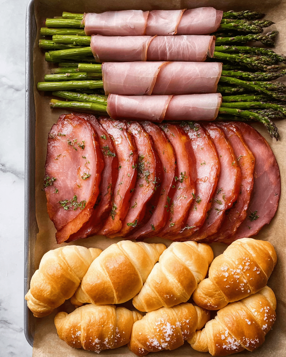 The image shows a rectangular tray lined with parchment paper holding three types of food items neatly arranged in rows. At the top, there are several green asparagus spears wrapped tightly with thin, pinkish slices of prosciutto, giving a mix of green and soft pink colors with slight twists in texture. Below the asparagus, a row of eight glossy, reddish-pink slices of cooked ham is laid out in a slightly overlapping pattern with visible herbs and glaze on the edges. At the bottom, there is a line of five golden-brown, soft, and fluffy crescent rolls sprinkled lightly with coarse salt, showing a smooth, slightly shiny crust. The tray rests on a surface with a white marbled texture. Photo taken with an iphone --ar 4:5 --v 7