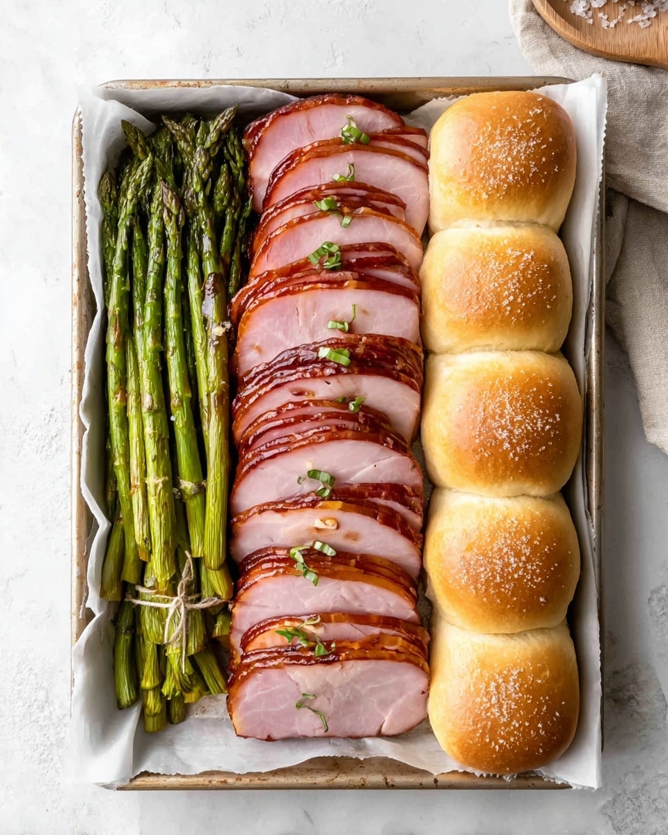 A rectangular tray lined with white parchment paper holds three distinct layers arranged side by side. On the left, green asparagus spears are wrapped tightly with thin slices of brown prosciutto, creating long, slender bundles. In the middle, there are nine evenly sliced pieces of ham with a light pink center and a darker, glazed, shiny brown crust, garnished with small green herb leaves and bits of toasted seasoning. On the right, there are six golden-brown soft dinner rolls, stacked in two columns, sprinkled lightly with coarse salt on top. The tray sits on a white marbled textured surface. photo taken with an iphone --ar 4:5 --v 7
