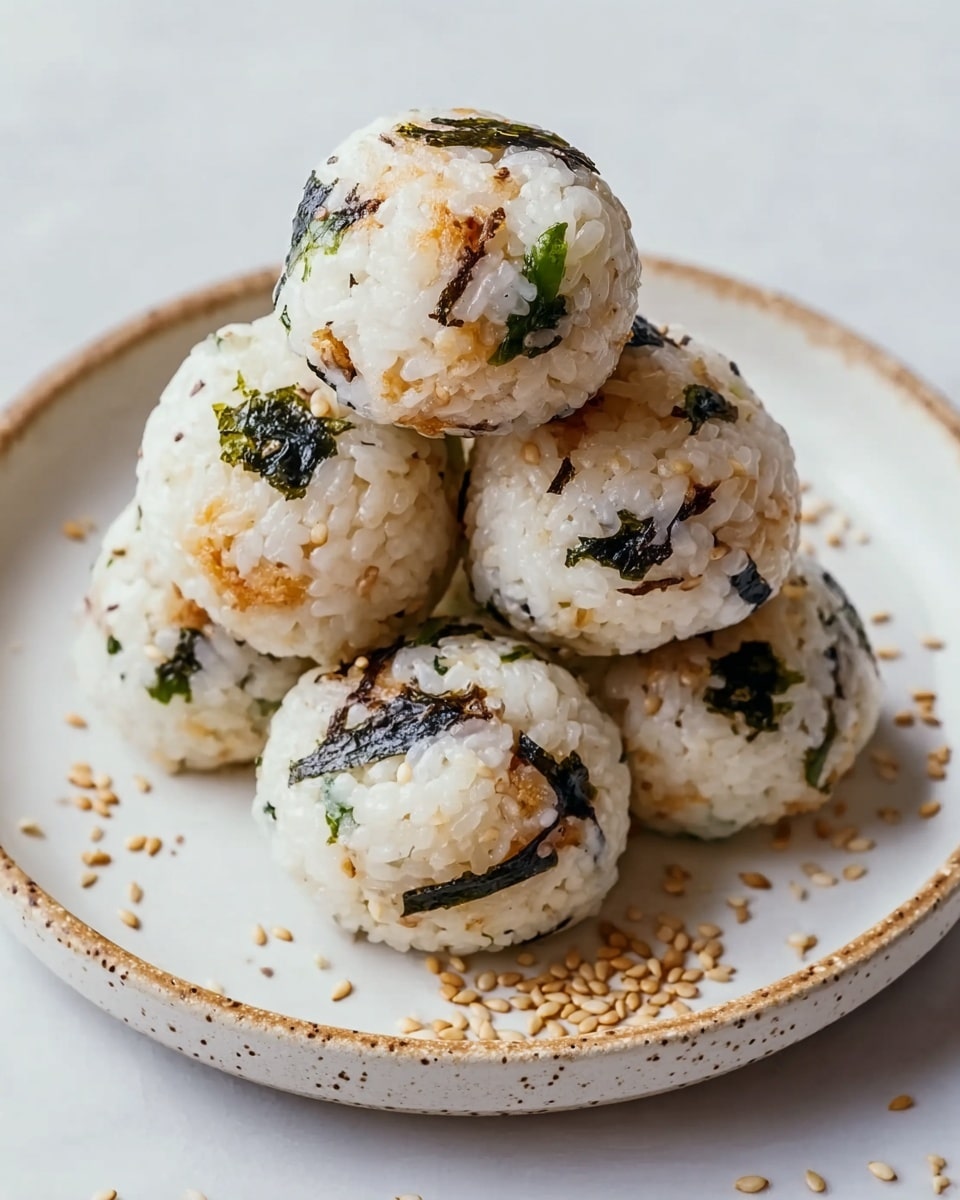 The image shows five round rice balls stacked together on a white plate with a speckled rim. Each rice ball is made of white rice mixed with small pieces of green seaweed and tan-colored sesame seeds scattered around and on top. The rice balls also have small patches of a light brown filling inside, visible through the rice. The plate rests on a white marbled texture surface, and a few sesame seeds are spread loosely around the rice balls. photo taken with an iphone --ar 4:5 --v 7