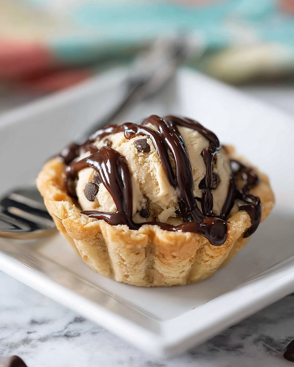 A close-up image of a dark gray metal muffin tray holding several baked chocolate chip cookie cups. Each cup features a one-layer golden brown, flaky crust forming the base and edge, with a rounded dome of light golden cookie dough filled with dark chocolate chips sitting inside. The cookie dough has a soft texture with cracks and chocolate chips visible on the surface. The background shows a white marbled texture. photo taken with an iphone --ar 4:5 --v 7