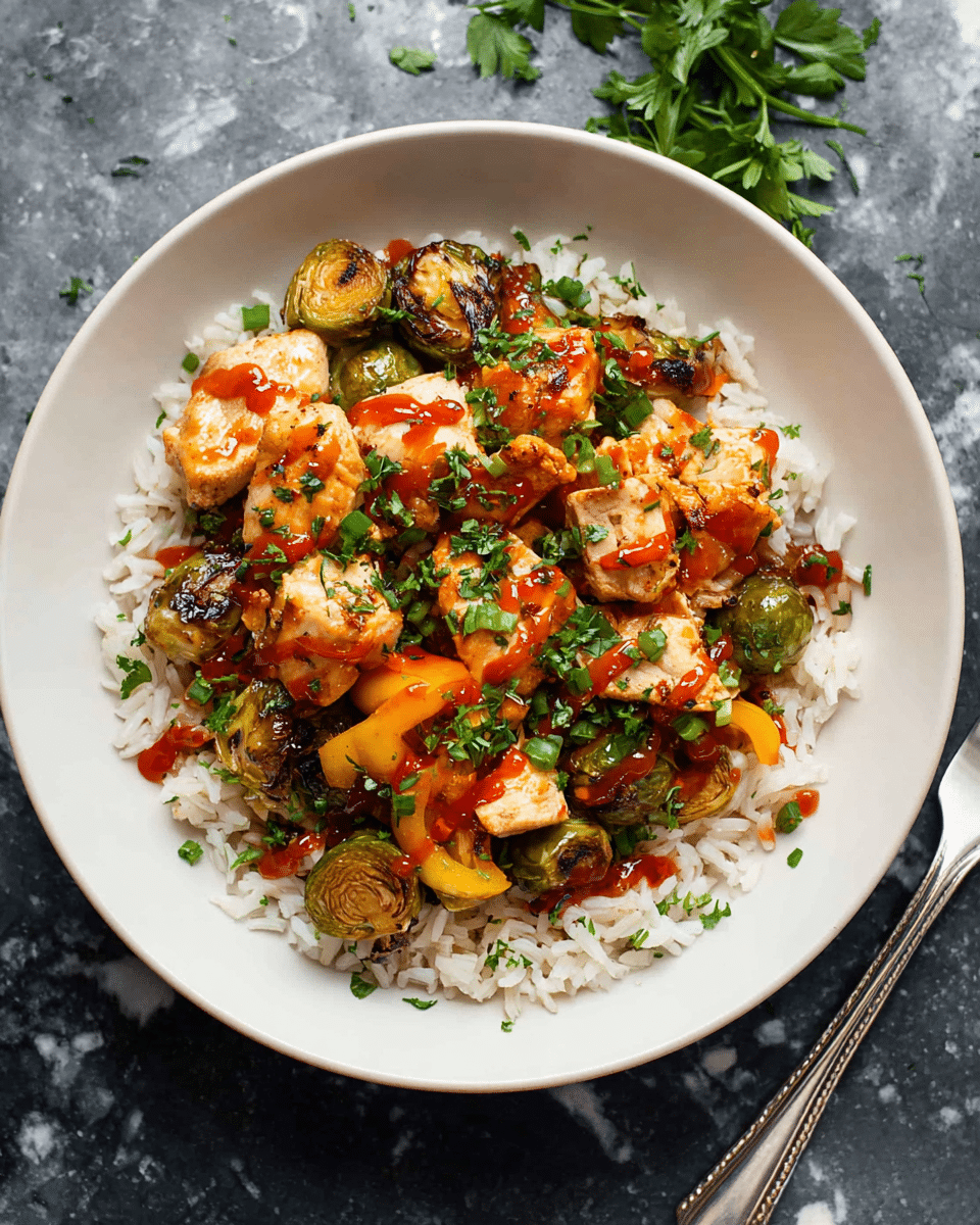 The dish shows a bowl of cooked white rice as the bottom layer, topped with roasted Brussels sprouts and slices of orange bell pepper that add green and orange pops of color. On top, there are golden-brown pieces of cooked chicken scattered around, drizzled with a shiny red chili sauce. Fresh chopped green herbs are sprinkled on the chicken and vegetables, giving a fresh look. The bowl is white, and the dish is placed on a white marbled surface with a silver fork on the right and green herbs in the background. Photo taken with an iphone --ar 4:5 --v 7