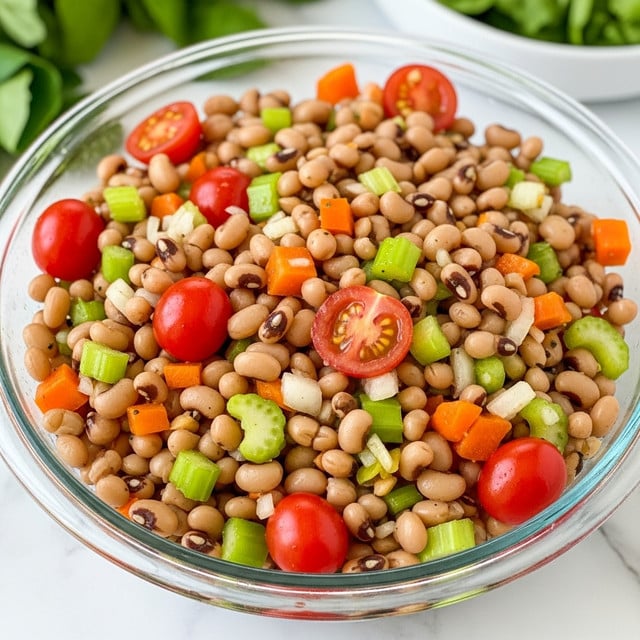 A clear glass bowl filled with a colorful salad composed mainly of light brown black-eyed peas with dark brown spots, mixed with bright red cherry tomato halves, small pieces of orange and green bell peppers, light green celery, and bits of white onion. The ingredients are evenly mixed, showing a fresh, healthy texture with a mix of smooth, soft beans and crisp vegetables. The bowl is placed on a white marbled surface with some green leafy vegetables blurred in the background. photo taken with an iphone --ar 4:5 --v 7