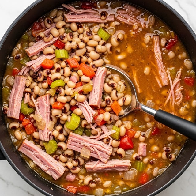 A close-up view of a pot filled with a colorful, chunky stew made of black-eyed peas, shredded pink ham pieces, and diced vegetables including green celery and red peppers, all mixed in a light brown broth; a silver and black spoon is partially submerged in the stew, stirring the ingredients together. The pot has dark edges, and the background shows a white marbled texture. photo taken with an iphone --ar 4:5 --v 7