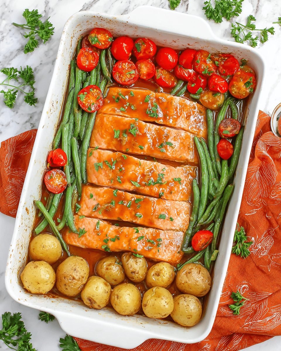The image shows a white baking dish with three clear layers of food: the top layer has four golden-orange salmon fillets coated with a shiny sauce and sprinkled with chopped green herbs; the middle layer consists of bright green beans mixed with halved red cherry tomatoes, both looking tender and slightly glossy; the bottom layer features halved roasted baby potatoes with a golden-brown skin and soft yellow inside, all placed on a white marbled surface with scattered parsley leaves around and an orange cloth nearby photo taken with an iphone --ar 4:5 --v 7
