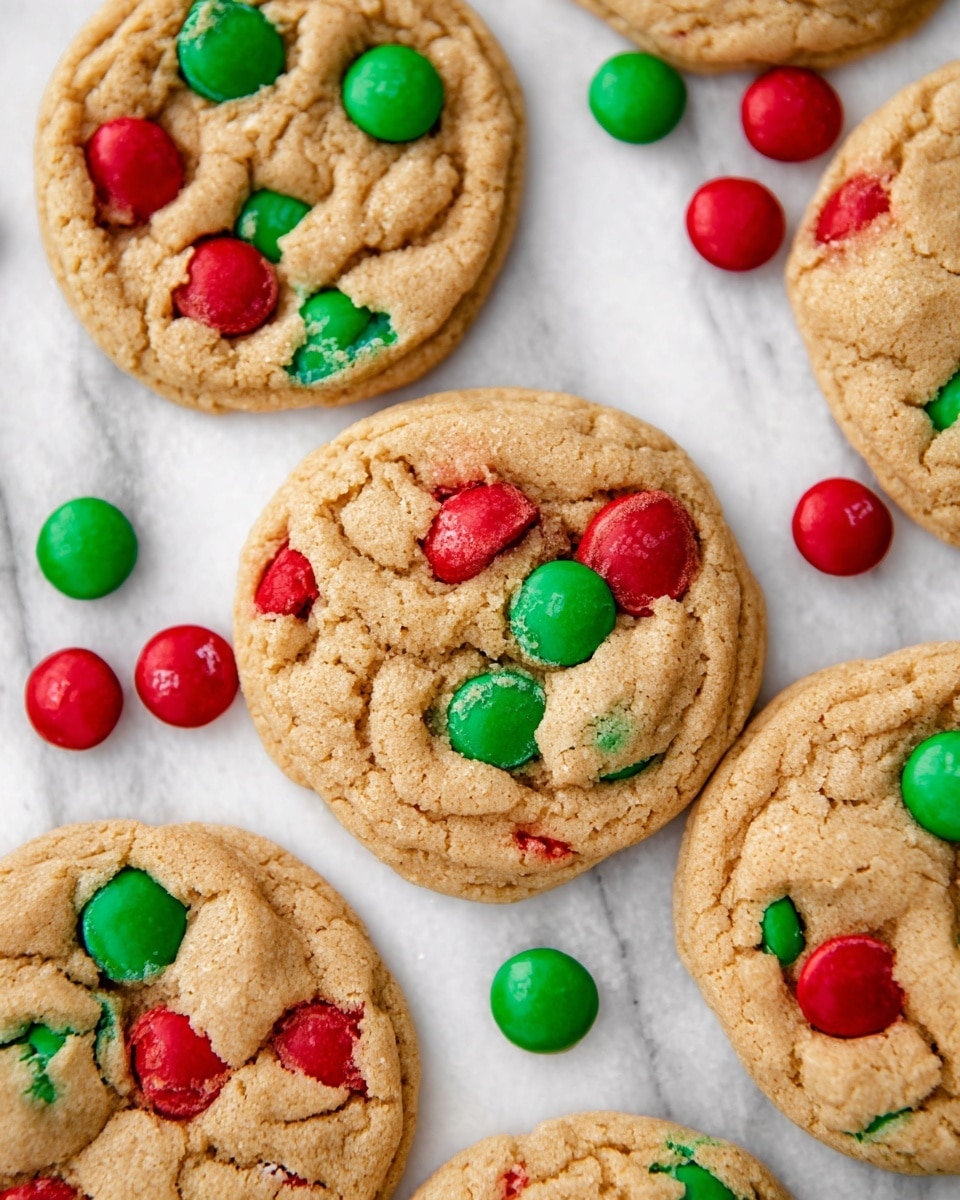 Several round cookies with a cracked, golden-brown surface are laid out on a white marbled texture. Each cookie contains embedded candy pieces in bright red and green, some partially broken, with additional loose red and green candies scattered around them. The cookies have a soft, slightly raised texture with a chewy look, and the colorful candies create a festive contrast against the warm, beige cookie dough. photo taken with an iphone --ar 4:5 --v 7