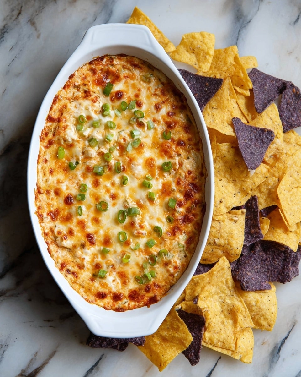 A white oval baking dish filled with a baked dip showing a golden-brown melted cheese layer on top, sprinkled with small pieces of green onions scattered across the surface; the cheese has a slightly bubbly and browned texture with hints of orange and white mixed in. Around the dish, there are many yellow and purple tortilla chips resting directly on a white marbled textured surface, providing a crunchy contrast to the creamy dip. photo taken with an iphone --ar 4:5 --v 7