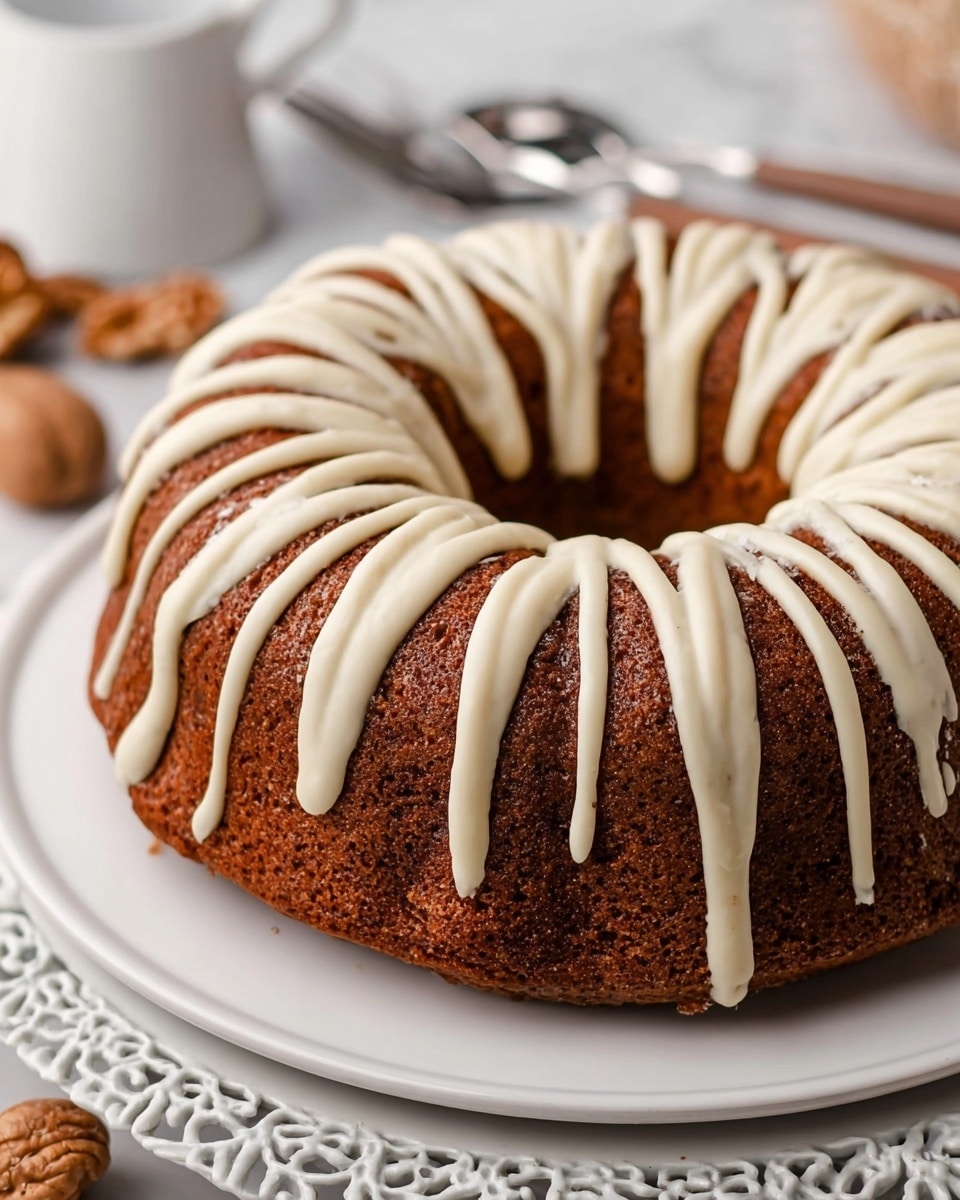 A round bundt cake with a rich brown color and a spongy texture sits on a white plate, which rests on a decorative edge charger. The top of the cake is decorated with thick white icing, drizzled in wide zigzag patterns around the whole cake, contrasting with the darker cake below. The background shows a softly blurred scene with a white marbled texture surface and some walnuts and silver cutlery nearby. The photo is clear and close-up, showing the moisture and crumb texture of the cake. photo taken with an iphone --ar 4:5 --v 7