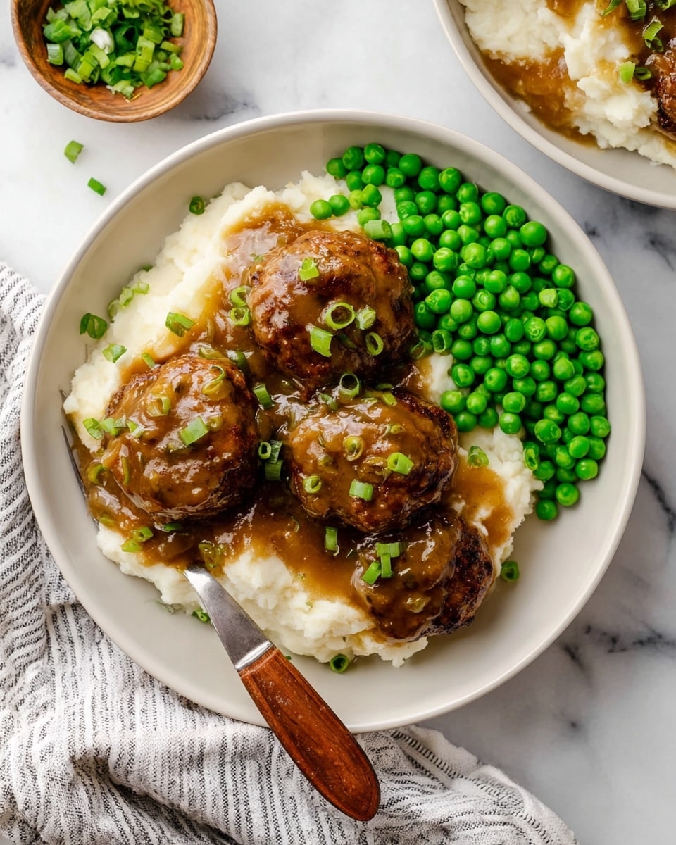 A white round plate holds a serving of mashed potatoes as the bottom layer, soft and creamy with a fluffy texture. On top, there are four brown meat patties covered in a thick, rich brown gravy with visible bits of onion, garnished with small green chopped scallions scattered across the meat. To one side of the plate, there is a pile of bright green peas adding a vibrant contrast to the dish. A wooden-handled spoon rests on the edge of the plate. The background is a white marbled surface with a striped cloth partially visible beside the plate. photo taken with an iphone --ar 4:5 --v 7