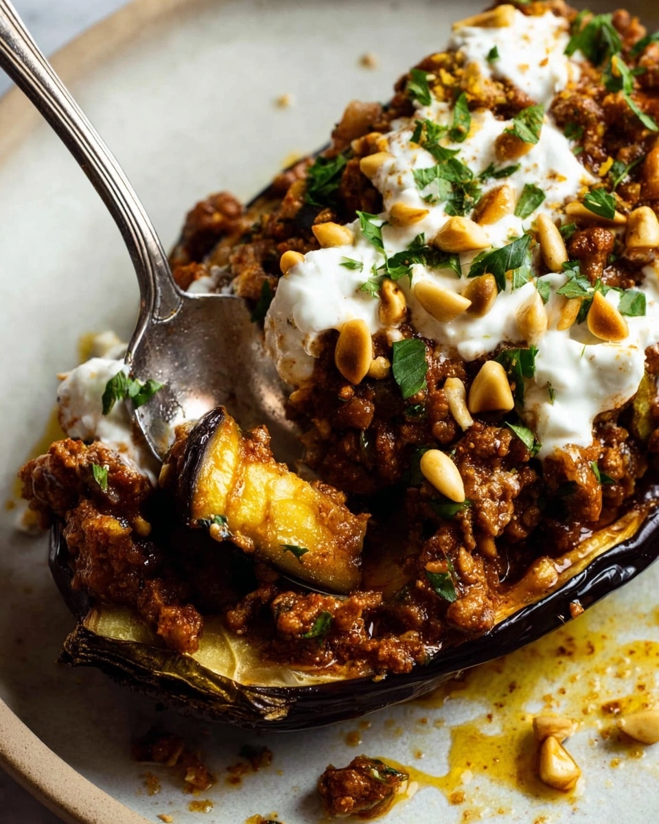 The image shows a close-up of a stuffed eggplant half filled with a rich brown meat mixture that has a soft, chunky texture. On top, there are dollops of white creamy sauce sprinkled with chopped green herbs and small golden pine nuts. A metal spoon is scooping a portion from the stuffed eggplant, revealing a piece of tender eggplant inside that is slightly glossy and yellowish. The eggplant sits on a white plate with some sauce spills and tiny bits of meat and pine nuts scattered around, all on a white marbled surface. photo taken with an iphone --ar 4:5 --v 7