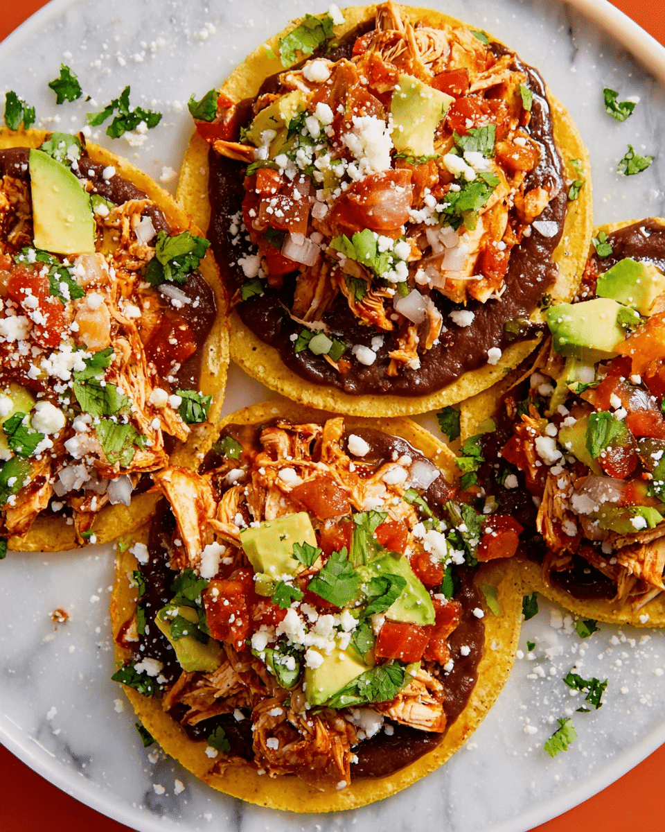 The image shows three tostadas arranged on a white plate, placed on a white marbled textured surface. Each tostada has three clear layers: the bottom is a golden yellow crispy corn tortilla, the middle is a thick spread of dark brown refried beans covering most of the tortilla, and the top layer has shredded orange-brown chicken mixed with small chopped white onions, bright green avocado chunks, red tomato salsa, and fresh green cilantro leaves scattered on top. Crumbled white cheese sprinkles are lightly spread across the tostadas and the plate. Photo taken with an iphone --ar 4:5 --v 7