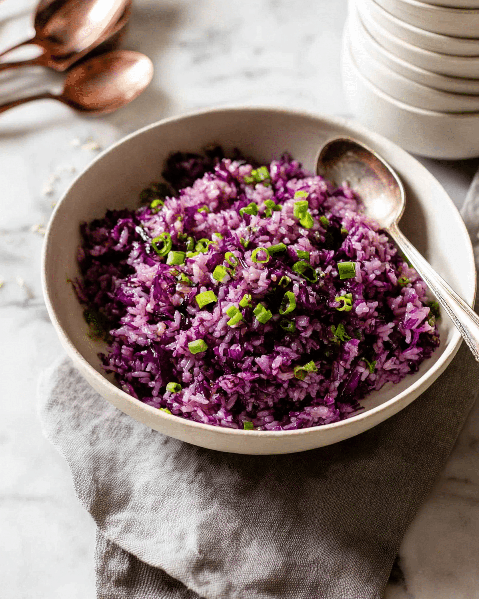 A white bowl filled with a purple rice dish mixed with shredded purple cabbage, giving the rice a vibrant purple color. There are small green onion slices scattered on top, adding a touch of green contrast. A silver spoon is placed inside the bowl on the right side, slightly buried in the rice. The bowl sits on a textured light grey cloth on a white marbled surface, with a few green onion slices scattered nearby. Photo taken with an iphone --ar 4:5 --v 7