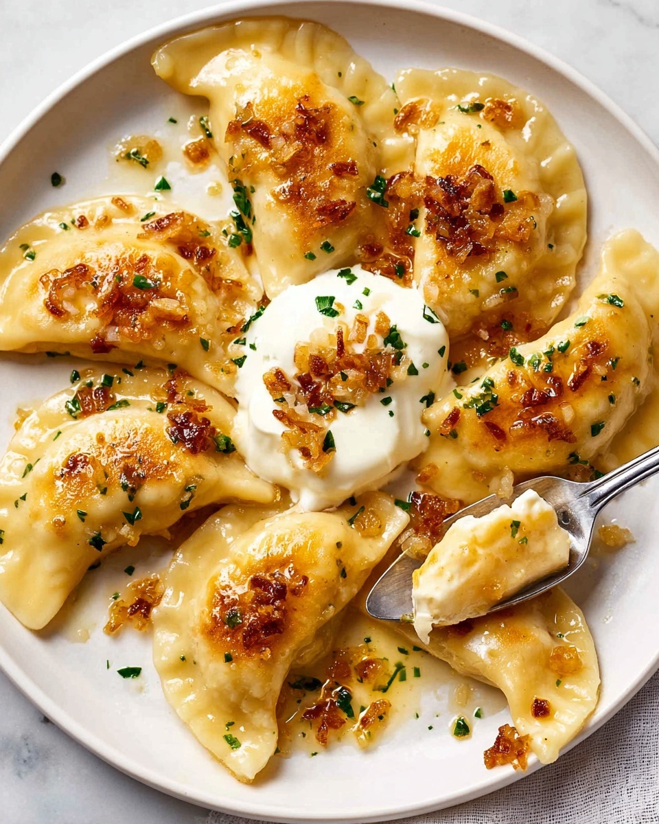 A white plate on a white marbled surface holds seven golden pierogi dumplings, each half-moon shaped with a smooth, slightly shiny dough. The dumplings are topped with crispy browned bits of sautéed onions and small green herb pieces scattered around. In the center, one pierogi is covered with a dollop of creamy white sour cream, garnished with a few chopped green herbs. A spoon lifts one pierogi, showing its plump center and glistening surface covered in butter and onion bits. photo taken with an iphone --ar 4:5 --v 7