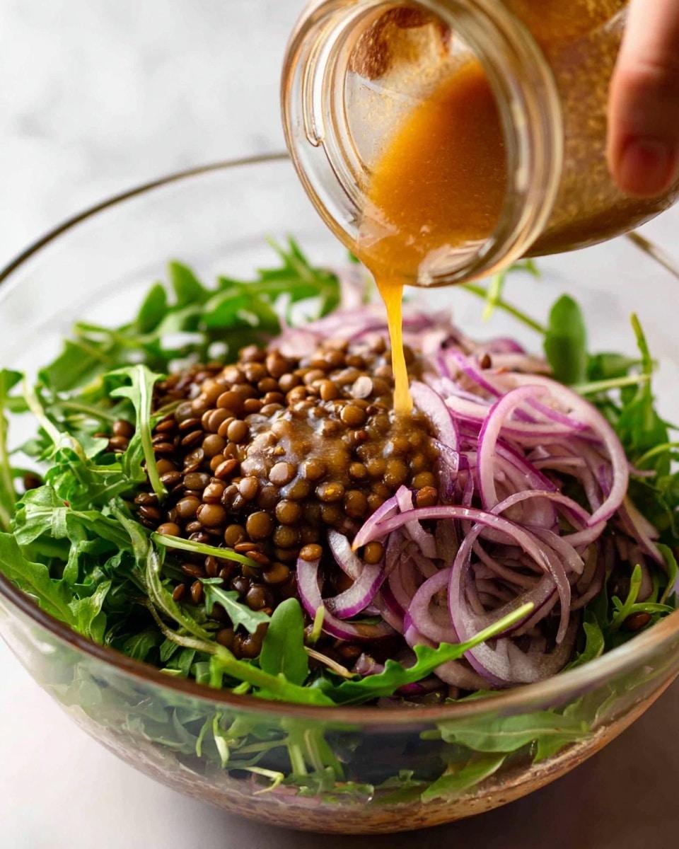 A clear glass bowl is filled with a fresh salad, starting with a base of dark green arugula leaves, layered with brown lentils and thinly sliced purple-red onions scattered on top. A woman's hand is seen pouring a thick, golden-brown dressing from a small clear jar, pouring over the lentils in the center of the bowl. The background surface is a white marbled texture. The image is close up, focusing on the pouring action and the colorful textures of the salad layers photo taken with an iphone --ar 4:5 --v 7