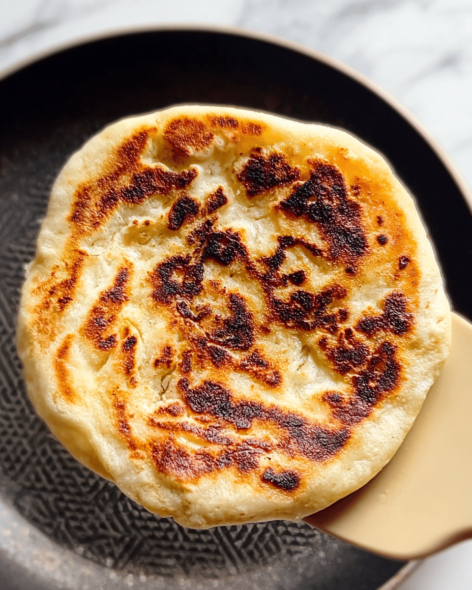 A toasted sandwich cut in half is held by woman's hand, showing its layers clearly. The outside bread is golden brown with some char marks, giving it a crispy texture. Inside, there are two main filling layers: a creamy white melted cheese base and a thick, shiny red jam spread on top. Fresh green cilantro leaves are placed inside, adding a touch of bright green color and a fresh texture. The sandwich is held over a white marbled surface, and some cilantro pieces are seen scattered below. Photo taken with an iphone --ar 4:5 --v 7