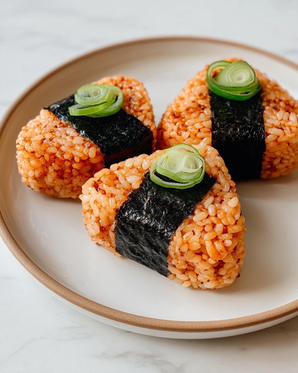 The image shows three triangular-shaped onigiri made of reddish-orange rice, each wrapped with a thick strip of dark seaweed around the middle. On top of each onigiri, there are thin slices of green onion as garnish. They are placed on a round white plate with a subtle beige rim, resting on a white marbled surface. The rice texture is well-defined and slightly glossy, and the seaweed has a smooth, slightly shiny appearance. photo taken with an iphone --ar 4:5 --v 7