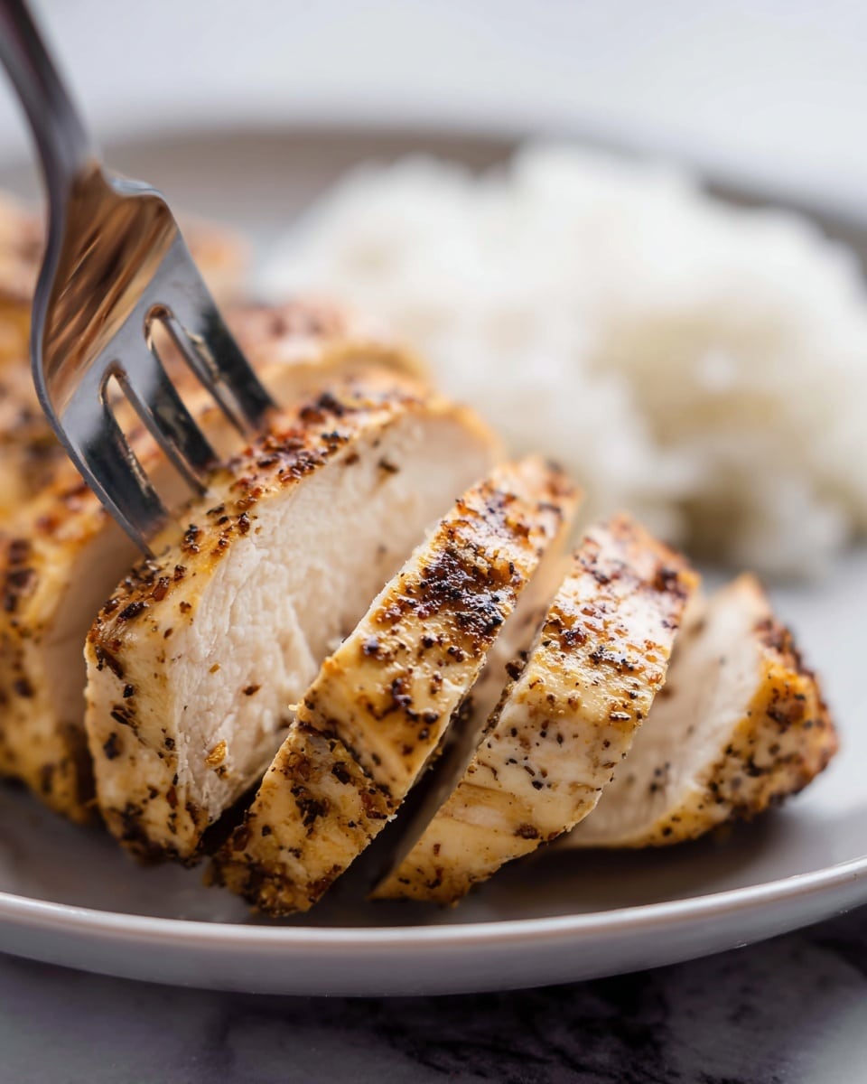A close-up view of a sliced chicken breast arranged in a row on a white plate. The chicken has a golden-brown color with black pepper and seasoning speckled all over the surface, giving it a coarse texture. The inside of the chicken is off-white and looks tender and juicy. A silver fork held by a woman's hand holds one piece of the chicken near the center of the image. In the background, there is a small pile of white rice, blurred slightly, sitting on the same white plate. The scene is set on a white marbled texture, creating a clean and bright atmosphere. photo taken with an iphone --ar 4:5 --v 7