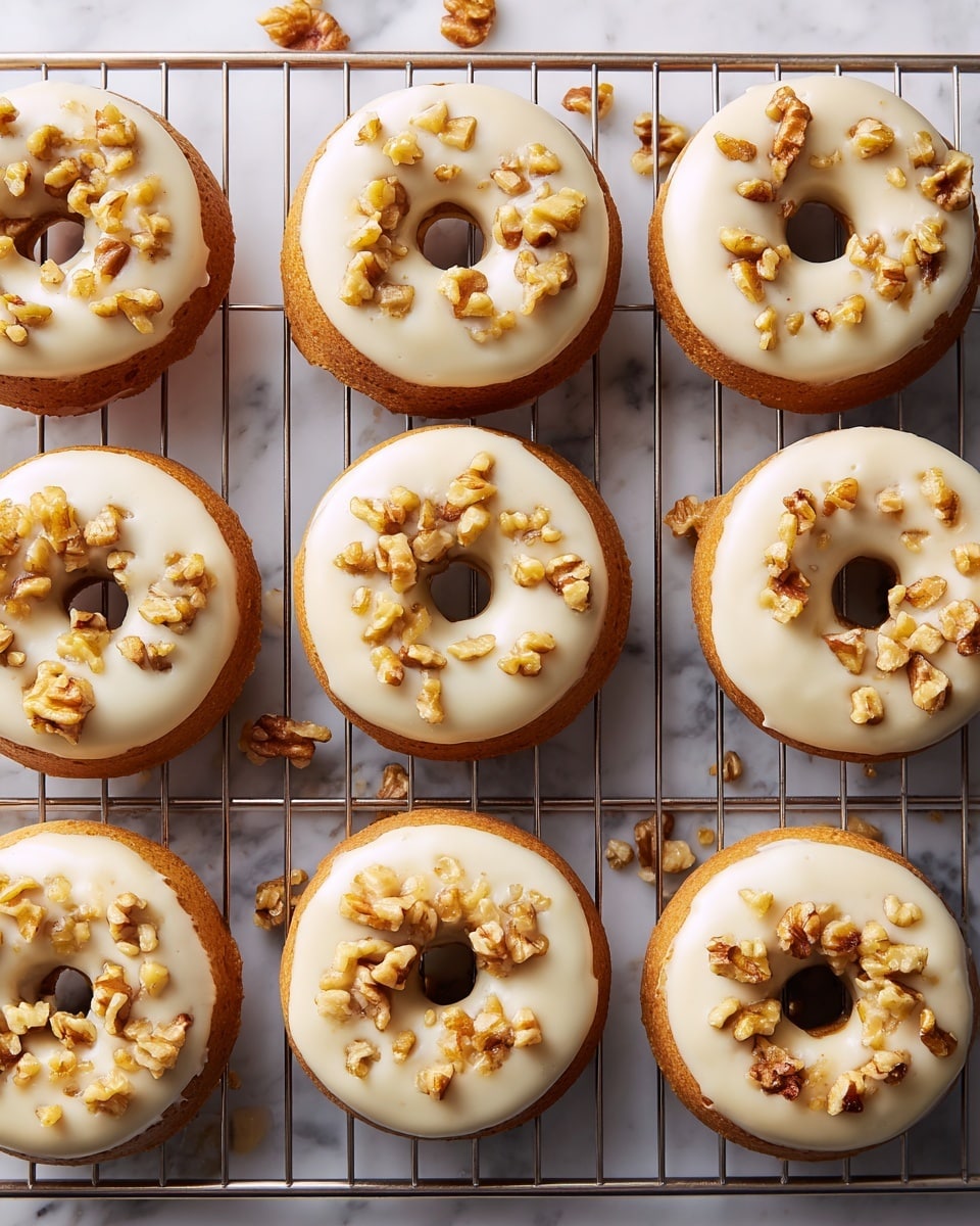 The image shows nine round donuts arranged on a metal cooling rack placed over a white marbled surface. Each donut has a light golden brown base layer, topped with a smooth, creamy white icing that covers the entire upper surface. On top of the icing, there are small, uneven chunks of toasted walnuts scattered across each donut, adding texture and a touch of light brown color. The donuts are evenly spaced in a grid-like pattern, and a few walnut pieces are also visible on the rack and marble surface around the donuts. photo taken with an iphone --ar 4:5 --v 7
