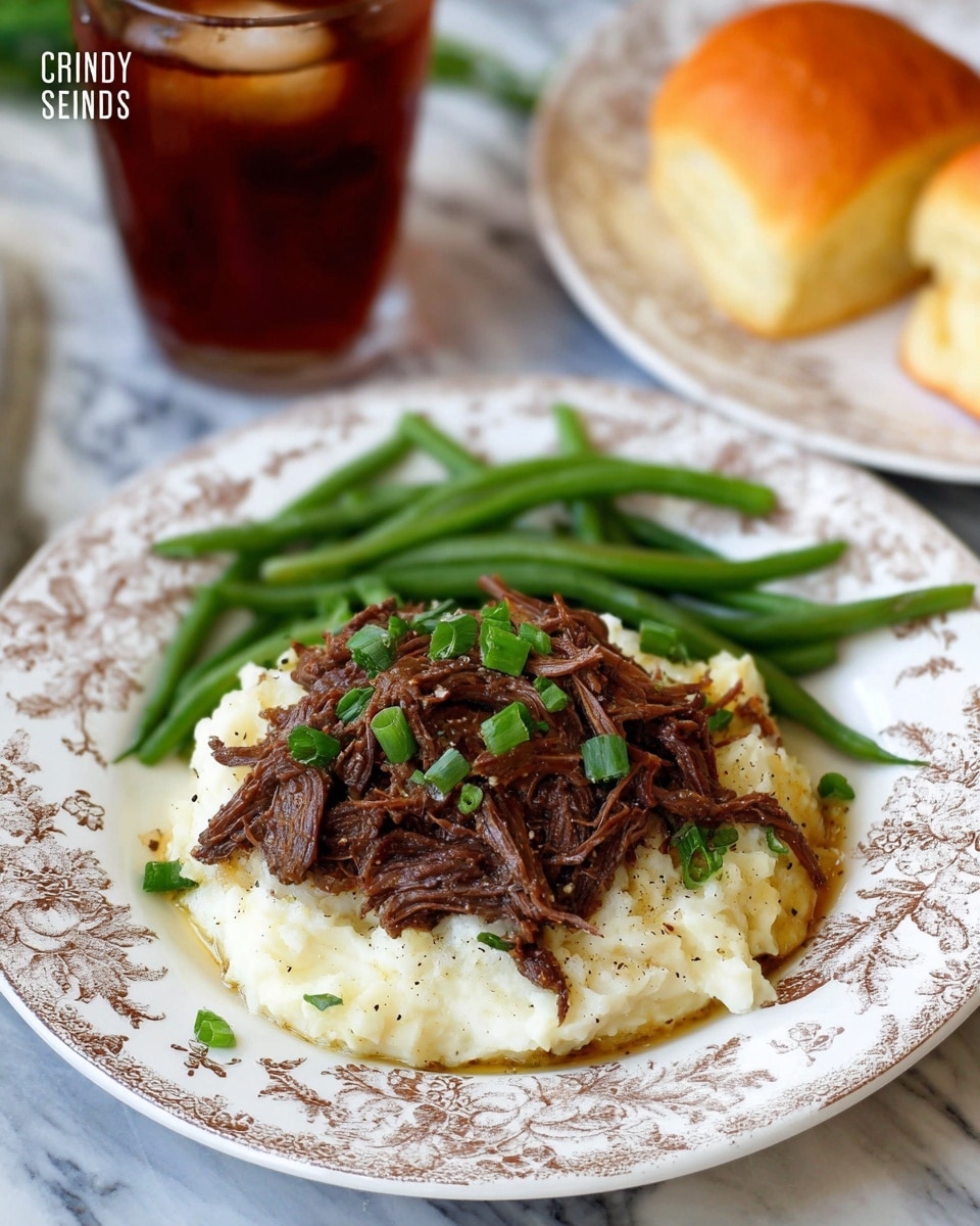 The image shows a white plate with a detailed floral pattern holding a well-arranged meal. At the bottom layer is a creamy white mashed potato base with a smooth texture and slight seasoning of black pepper visible. On top of the mashed potatoes, there is a layer of dark brown shredded beef, garnished with small bright green chopped herbs, likely green onions. To the left side of the plate, there is a serving of fresh green beans with a glossy surface indicating they are cooked but still crisp. On the right side of the plate, there is a soft, golden brown dinner roll with a shiny surface. In the background, there is a glass of iced dark red drink on a white marbled surface. photo taken with an iphone --ar 4:5 --v 7