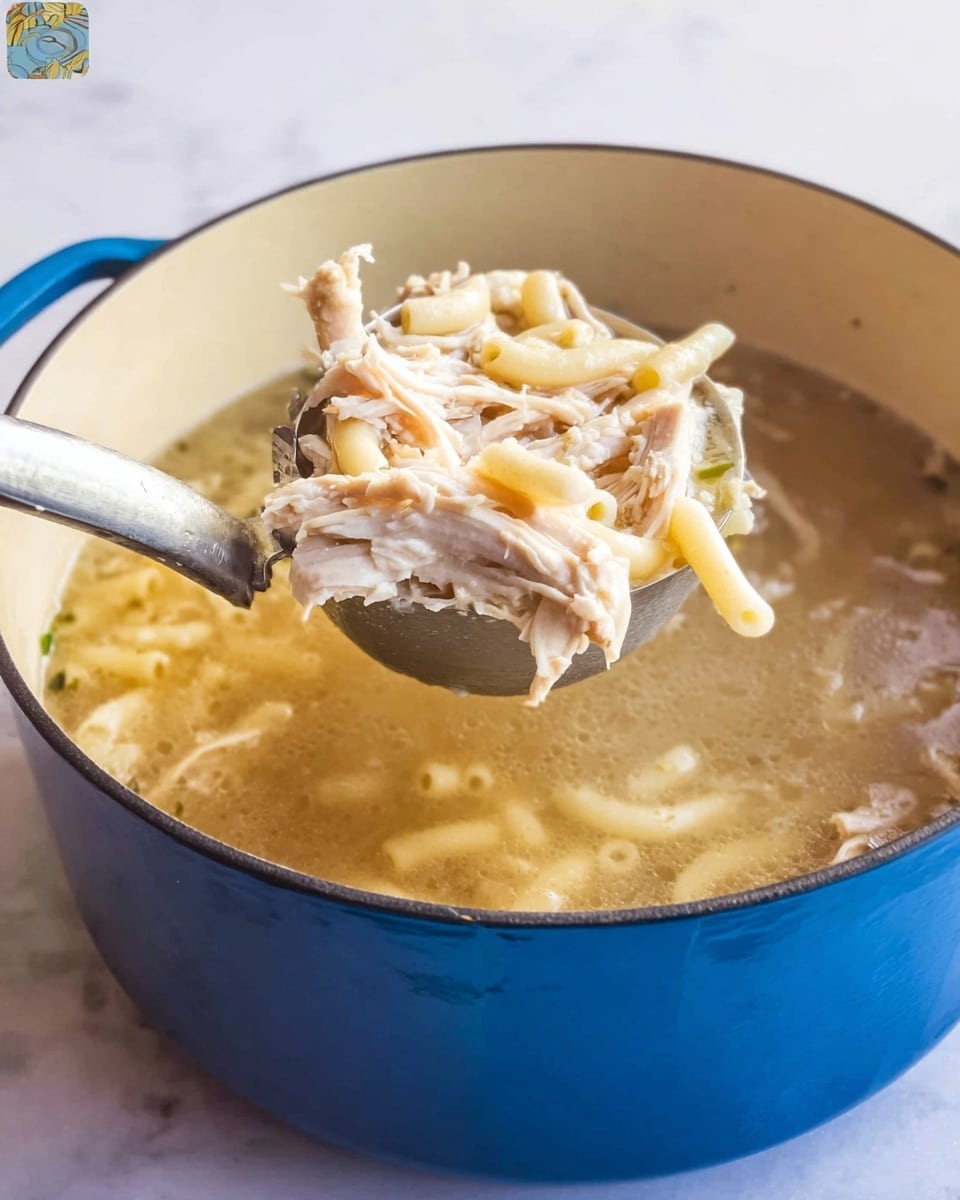 A close-up of a large blue pot filled with clear broth soup containing shredded white chicken and pale macaroni pasta. A metal ladle is lifting a scoop of the soup showing a mix of soft, shredded chicken on top of short tubular macaroni noodles, all in a light broth. The pot is set on a white marbled surface, and the texture inside the pot is smooth and shiny. photo taken with an iphone --ar 4:5 --v 7