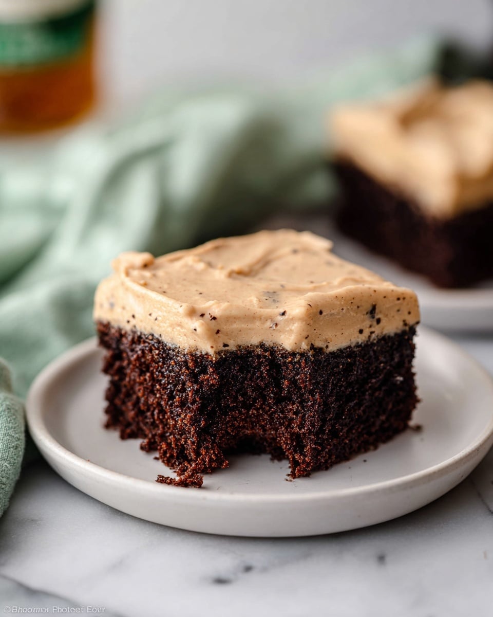 A batch of nine square chocolate brownies is shown on a sheet of parchment paper placed on a white marbled texture. Each brownie is topped with a thick layer of light brown frosting that is smooth with visible swirls and tiny dark specks throughout. One brownie in the front has a bite taken out of it, revealing a dense, moist interior. The brownies are arranged close together, with clear straight cuts separating each piece. The image captures the soft and creamy texture of the frosting contrasting with the rich chocolate base. Photo taken with an iphone --ar 4:5 --v 7