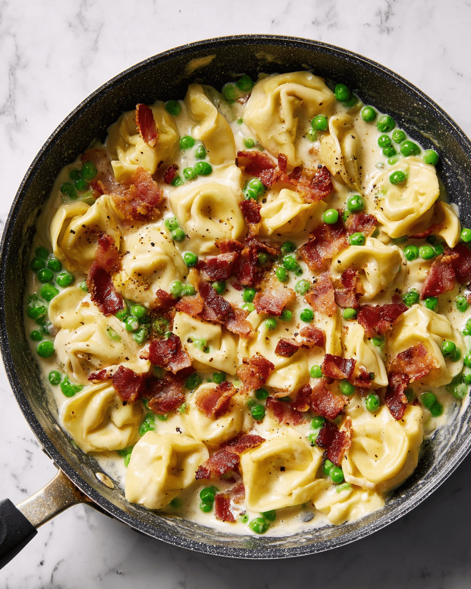 The image shows a close-up of a black pan filled with three layers: the bottom layer is a creamy white sauce, the middle layer holds light yellow tortellini pasta with a smooth texture, and the top layer is dotted with bright green peas and crispy, reddish-brown bacon pieces scattered evenly. The pan handle extends to the right side, placed on a white marbled surface. photo taken with an iphone --ar 4:5 --v 7