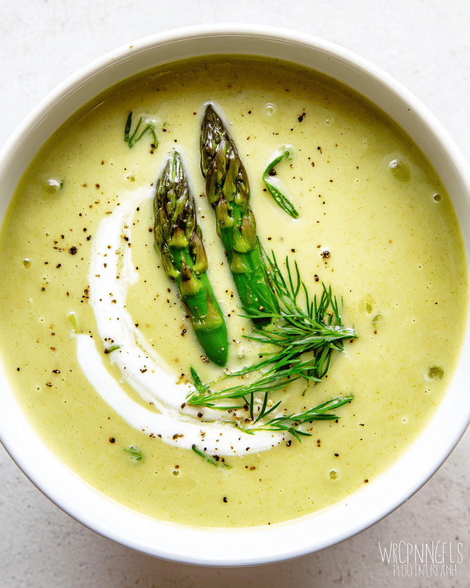 A white bowl filled with light green creamy soup, smooth in texture with small specks of black pepper scattered over the surface, topped with two whole green asparagus tips placed near the center, and a small bunch of fresh green dill resting beside the asparagus. There is a swirl of white cream on top of the soup adding contrast. The bowl sits on a white marbled surface. photo taken with an iphone --ar 4:5 --v 7