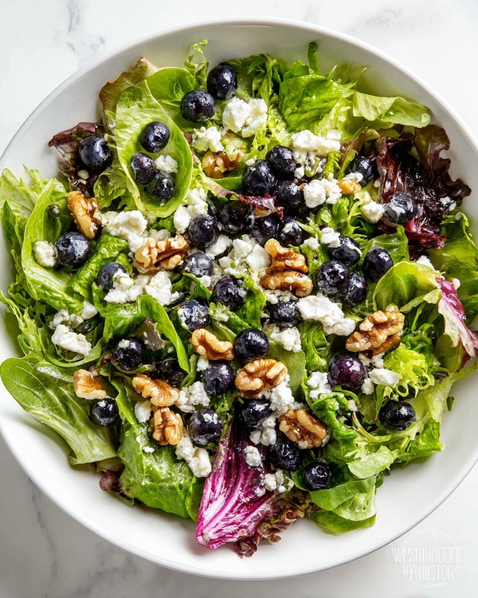A white bowl filled with a fresh salad showing three main layers: the bottom layer is mixed green and red lettuce leaves, the middle layer has fresh blueberries scattered all over, and the top layer is crumbled white cheese and small chopped walnuts adding texture and color contrast. The bowl is placed on a white marbled surface, surrounded by a smaller white bowl of whole blueberries on the right, a partial white bowl of more salad at the top left, and a glass container with pink salad dressing toward the bottom left. A silver fork is placed near the bottom left corner. Photo taken with an iphone --ar 4:5 --v 7