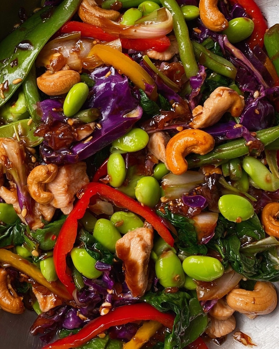 A black pan holds a colorful stir-fry with many layers of ingredients, starting with pieces of cooked chicken scattered evenly. Mixed with the chicken are long slices of red, yellow, and orange bell peppers adding bright colors, along with light green sugar snap peas and edamame beans spread on top. There are also chunks of deep purple cabbage and green onion pieces filling the dish. A wooden spoon rests on the right side of the pan, partially under the stir-fry. The pan sits on a white marbled surface next to a soft beige cloth. photo taken with an iphone --ar 4:5 --v 7