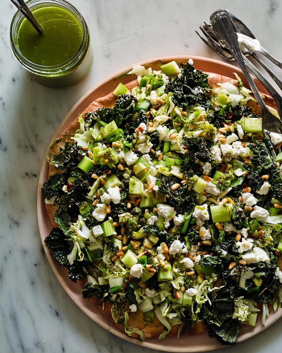 A large round flatbread is topped with a mixed green salad featuring dark, leafy kale and lighter chopped cabbage as the base layer. Scattered across the greens are small cubes of pale green cucumber and bits of bright green scallions. White crumbles of fresh cheese are spread evenly on top, adding a soft texture. Tiny tan pine nuts are sprinkled throughout, adding crunch. Drops of green herb dressing are drizzled over the whole dish. The flatbread sits on a white marbled surface, with an open glass jar of green dressing nearby, and two metal forks resting on the edge of the flatbread. Photo taken with an iphone --ar 4:5 --v 7