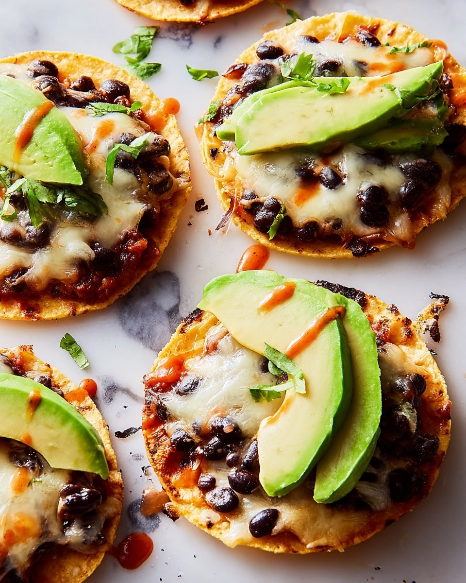The image shows several small round tostadas on a white marbled surface. Each tostada has three main layers: a golden crispy tortilla base, a layer of melted white cheese mixed with black beans scattered unevenly, and on top, three slices of fresh bright green avocado placed in a fan shape. There is a light drizzle of reddish sauce over the avocado and cheese, adding small spots of color. Some black beans and bits of melted cheese are scattered on the surface around the tostadas. photo taken with an iphone --ar 4:5 --v 7