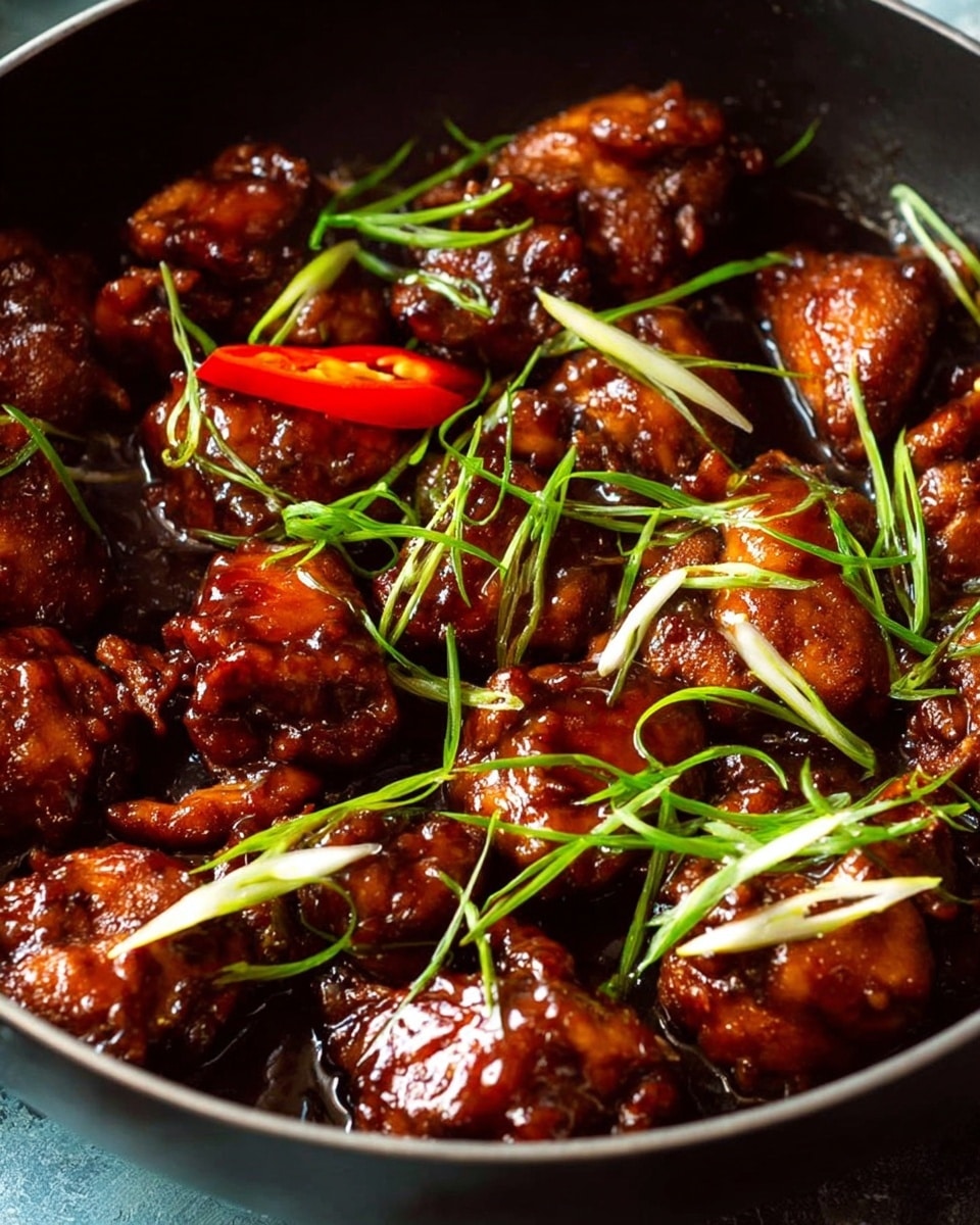 The image shows a close-up view of a dish in a black pan filled with several pieces of dark brown glazed chicken, coated evenly in a shiny, rich sauce. The chicken pieces are nestled closely together with a glossy texture. On top, thin, light green strands of scallions and white root slices add freshness and contrast. There is also a red chili pepper cut in half, showing white seeds inside, placed toward the center-left area, adding a pop of bright color. The overall look is warm and appetizing with deep brown and green tones. photo taken with an iphone --ar 4:5 --v 7