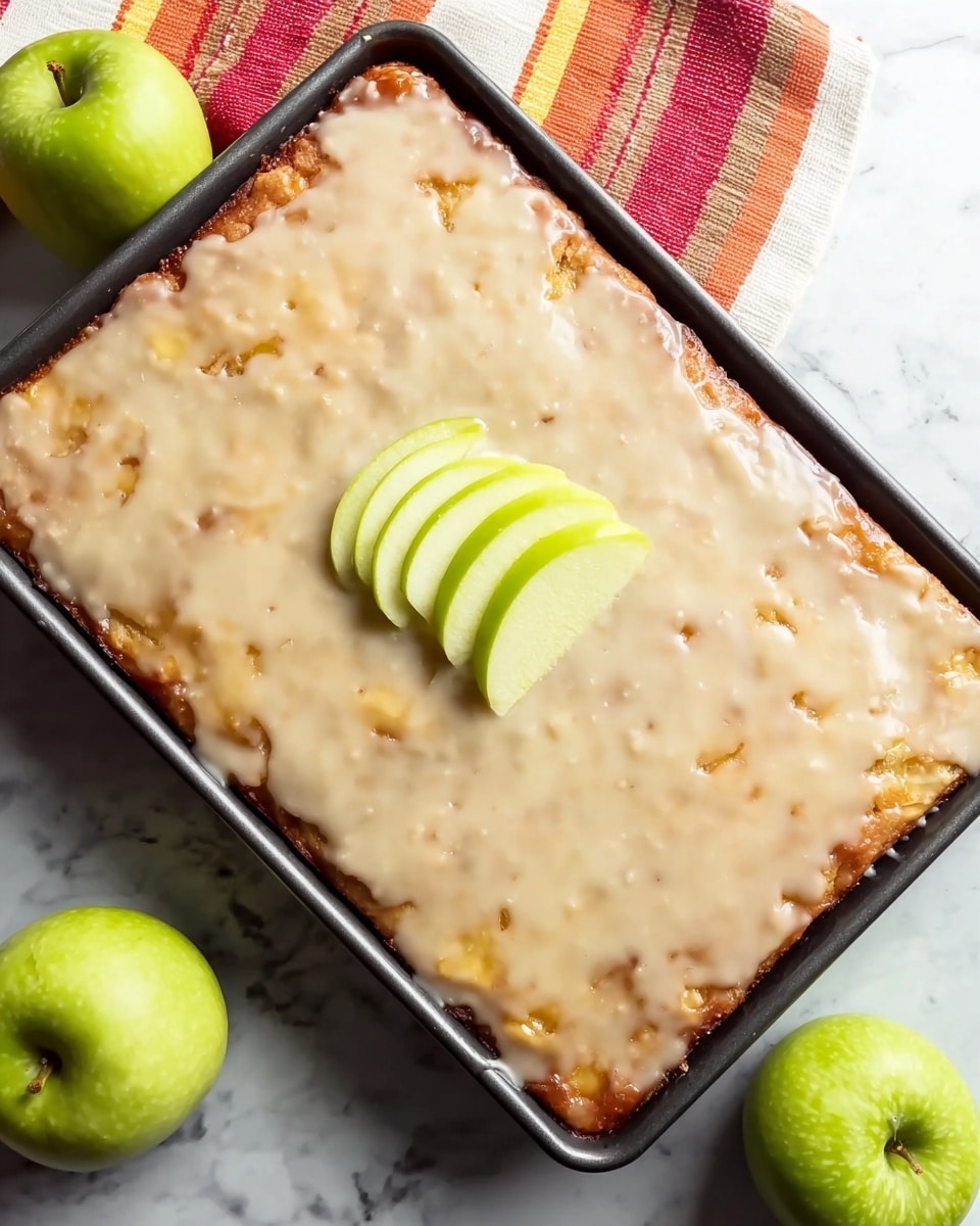 A freshly baked rectangular apple dessert sits in a black baking tray, covered with a smooth, shiny light beige glaze that spreads evenly across the top with small golden-brown spots peeking through. In the center, five thin slices of bright green apple are neatly arranged like a fan as a simple garnish. The tray rests on a white marbled surface with two whole green apples and one apple half placed nearby, along with a striped cloth in red, orange, and white tones tucked in the background. Photo taken with an iphone --ar 4:5 --v 7