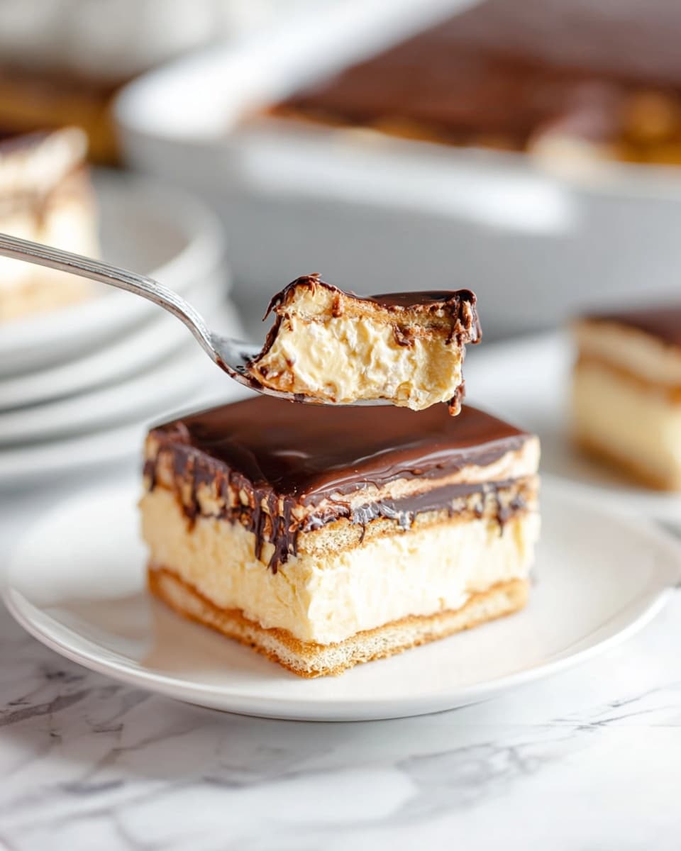 A close-up image shows a square dessert with three visible layers: the bottom and middle layers are light brown wafer-like cookies, the second and fourth layers are creamy light yellow custard, and the top layer is a smooth, glossy dark chocolate coating. A spoon holds a bite-sized piece of the dessert, clearly showing these layers. The dessert sits on a white plate placed on a white marbled surface. In the background, a baking dish with the remaining dessert and some blurred plates can be seen. Photo taken with an iphone --ar 4:5 --v 7