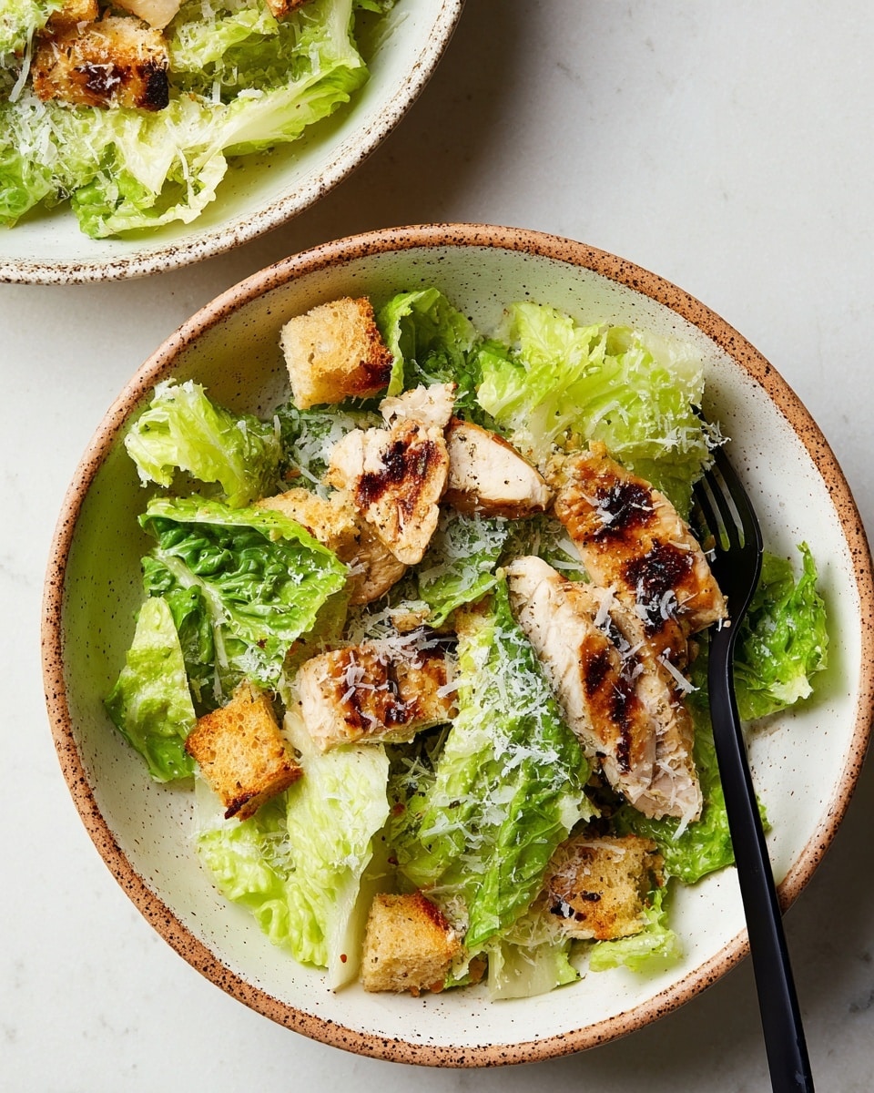 A bowl filled with fresh green romaine lettuce leaves as the base layer, topped with pieces of grilled chicken showing char marks and a golden-brown color. Scattered across the lettuce are golden, crispy croutons adding texture, while finely grated white cheese lightly covers the chicken and some lettuce pieces. A black fork rests on the side inside the bowl, which is white with brown speckled edges. The bowl sits on a white marbled surface. photo taken with an iphone --ar 4:5 --v 7