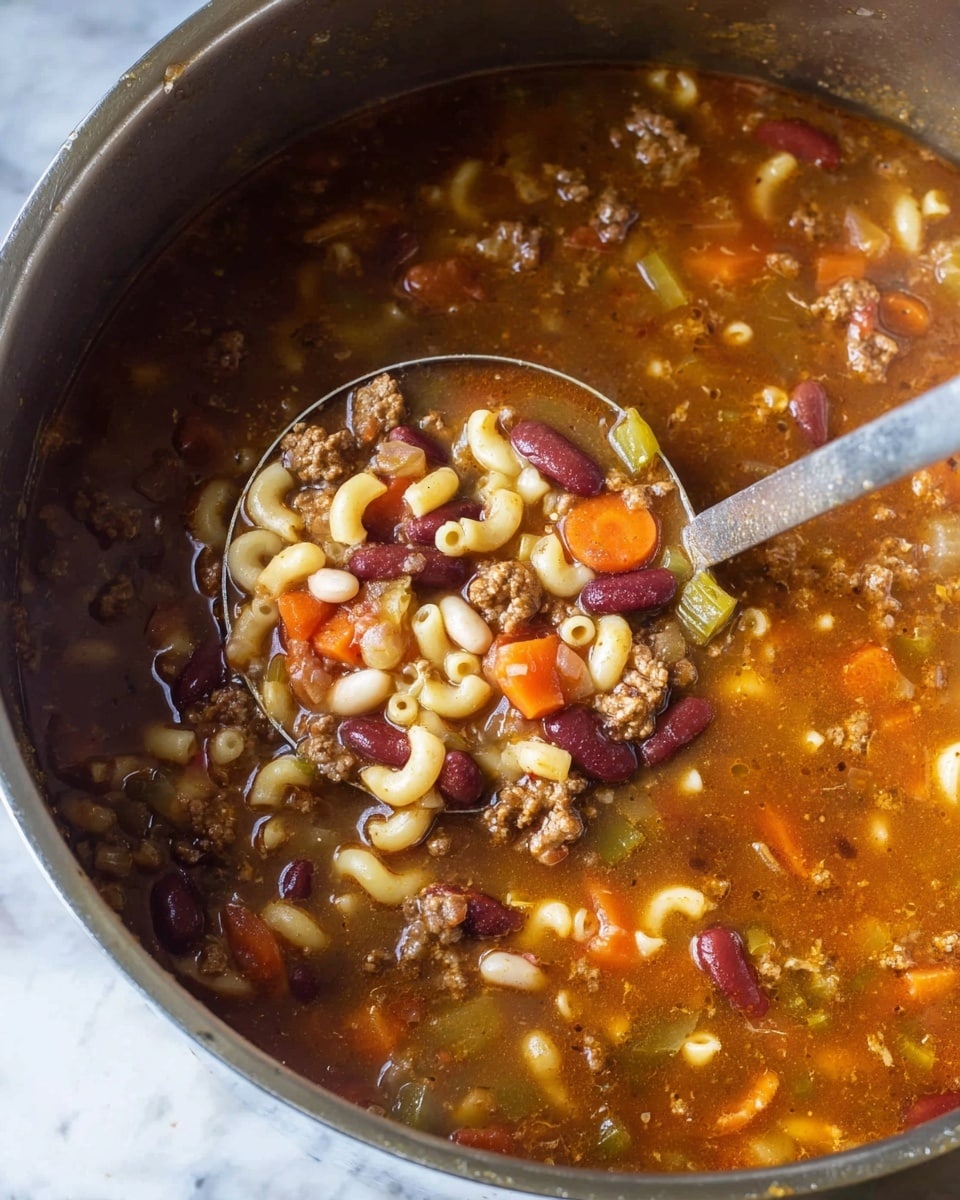 A close-up view of a large metal pot filled with a thick soup showing a mix of chunky ingredients. The soup has layers of small elbow pasta in pale yellow, whole kidney beans in dark red, white beans, brown cooked ground meat, and visible pieces of orange carrots and light green celery. The soup broth is brownish and slightly shiny, coating all the ingredients and filling the pot almost to the top. A large silver ladle scoops some of the soup, showing all layers clearly, with the soup glistening and textured. The background is a white marbled texture. photo taken with an iphone --ar 4:5 --v 7