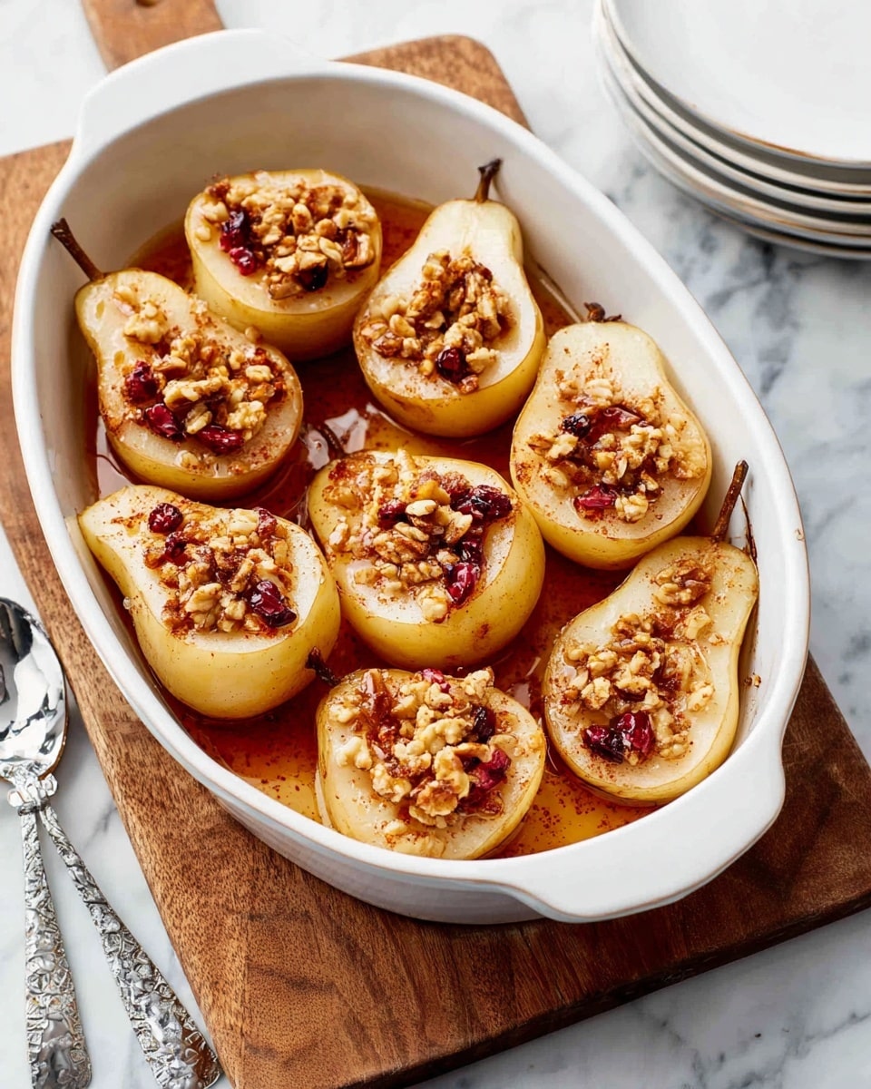 The image shows a white oval baking dish filled with eight halved pears arranged closely together, each pear cut side up. The pears have a light golden-yellow color with slightly darker edges from cooking. Each pear half has a hollowed-out center filled with granola pieces mixed with chopped walnuts and dried cranberries, giving a textured, chunky topping in shades of brown and red. A light cinnamon spice is sprinkled over the pears, and a thin layer of syrup or honey coats the bottom of the dish, adding a glossy amber shine. The baking dish rests on a wooden board on top of a white marbled surface, with a stack of white plates and a spoon with a patterned handle nearby. photo taken with an iphone --ar 4:5 --v 7