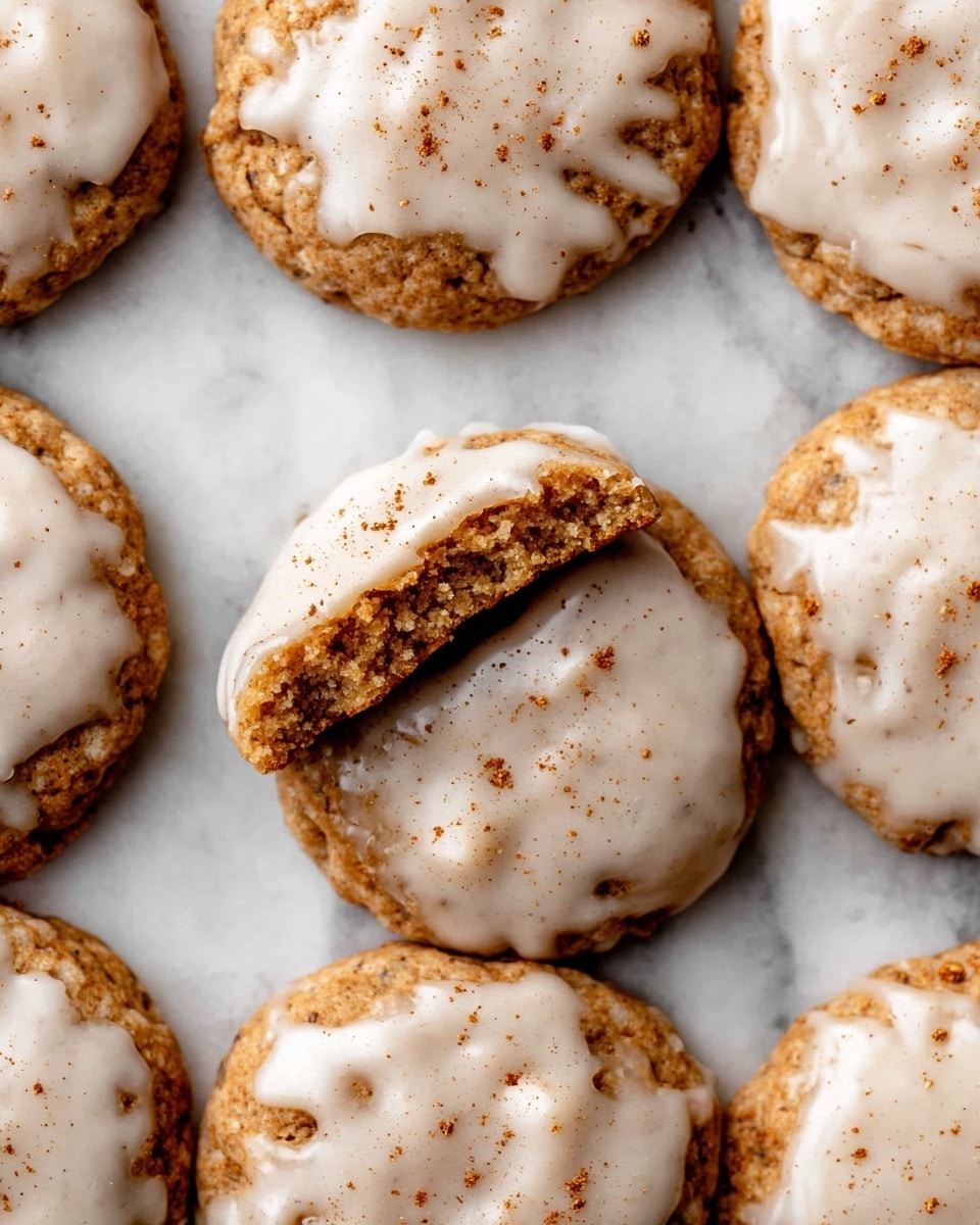 The image shows a close-up of several round cookies laid out on a white marbled surface. Each cookie has one layer of light brown, slightly rough textured dough, and a second uneven layer of white glaze spread on top. The glaze has a smooth, shiny look with a few small cracks and is sprinkled lightly with brown cinnamon or spice powder. One cookie in the top center is broken in half, showing the thick texture of the dough inside. photo taken with an iphone --ar 4:5 --v 7