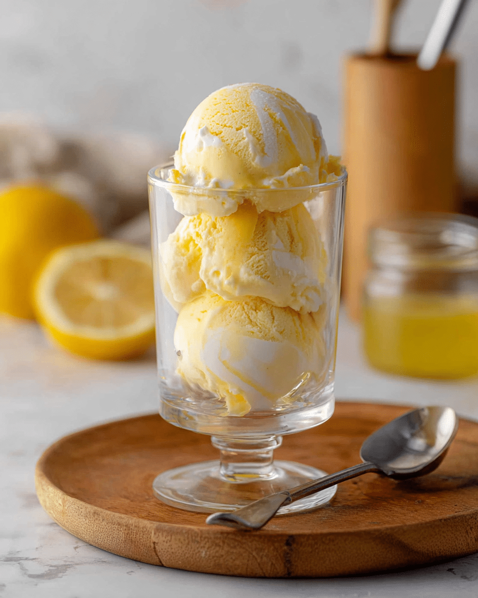 The image shows a clear glass cup filled with three scoops of yellow and white swirled ice cream stacked on top of each other, with creamy textures and some melting around the edges. The glass cup is placed on a round wooden board with a silver spoon resting beside it. In the background on the white marbled surface, there is a cut lemon, a small jar of yellow liquid, and a bamboo container with a metal utensil sticking out. The whole setting is softly lit, creating a fresh and inviting look. photo taken with an iphone --ar 4:5 --v 7