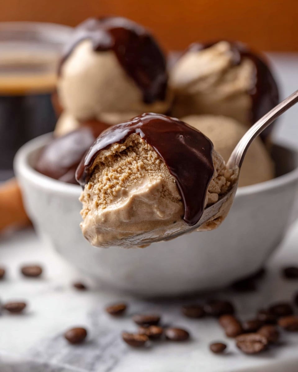 A close-up of a spoon holding a scoop of creamy, light brown coffee ice cream with a thick layer of dark chocolate partially covering the top. In the background, a white bowl filled with several scoops of the same coffee ice cream, some coated with dark chocolate, rests on a white marbled surface scattered with coffee beans. The ice cream has a smooth, velvety texture, and the dark chocolate layer looks glossy and rich, contrasting with the creamy base. Photo taken with an iphone --ar 4:5 --v 7