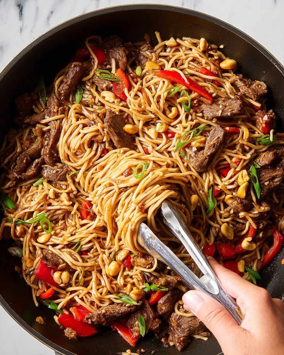 A black pan filled with a mix of thin, light brown noodles, dark brown cooked beef pieces spread evenly, bright red bell pepper chunks, scattered golden peanuts, and small green onion slices. A woman's hand holds silver tongs lifting a clump of noodles and beef from the pan. The noodles are glossy and intertwined with the other ingredients, creating a rich, colorful, and textured stir-fry look, set against a white marbled texture. photo taken with an iphone --ar 4:5 --v 7