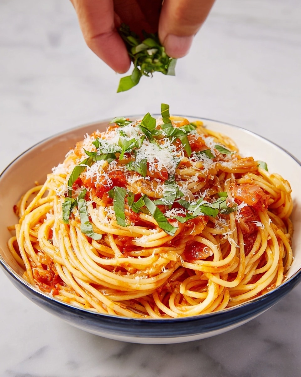 A white bowl filled with a serving of spaghetti topped with a light red tomato sauce mixed with small pieces of tomato and garlic, sprinkled generously with white grated cheese, and garnished with thin, bright green basil strips on top; a woman's hand is gently adding more fresh green basil from above, all set against a white marbled surface. photo taken with an iphone --ar 4:5 --v 7