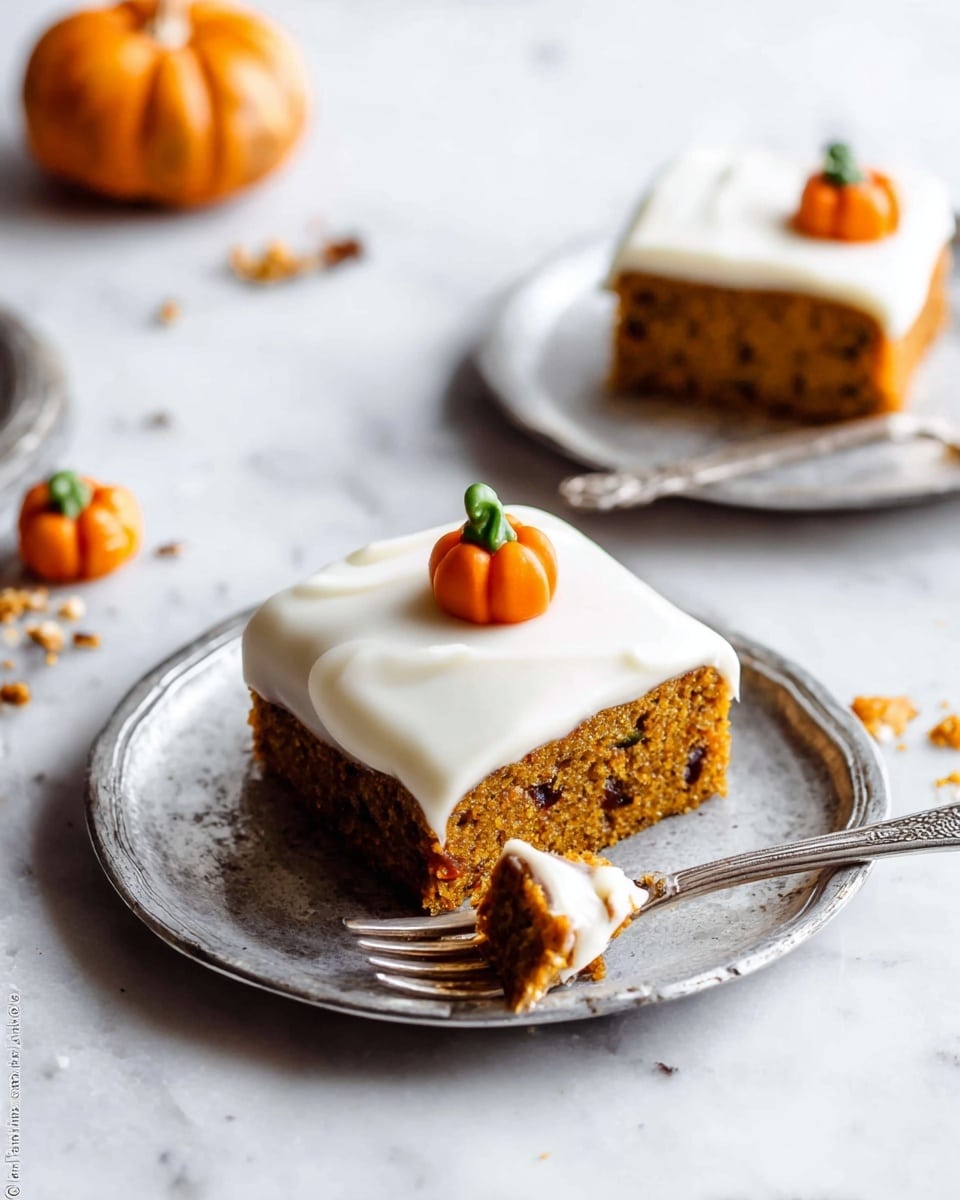 The image shows two pieces of pumpkin cake on white, slightly rustic plates with a silver finish. Each cake has one thick orange-brown layer filled with small darker bits and a thick smooth white frosting layer on top. On the center of the frosting of the closest cake, there is a small, bright orange pumpkin decoration with a green stem and a little brown detail. One piece has a bite taken out of the front corner, exposing the textured cake inside. A silver fork with a piece of cake and some frosting rests on the plate in front. The background is a white marbled surface with some crumbs and a small pumpkin decoration scattered around. Photo taken with an iphone --ar 4:5 --v 7