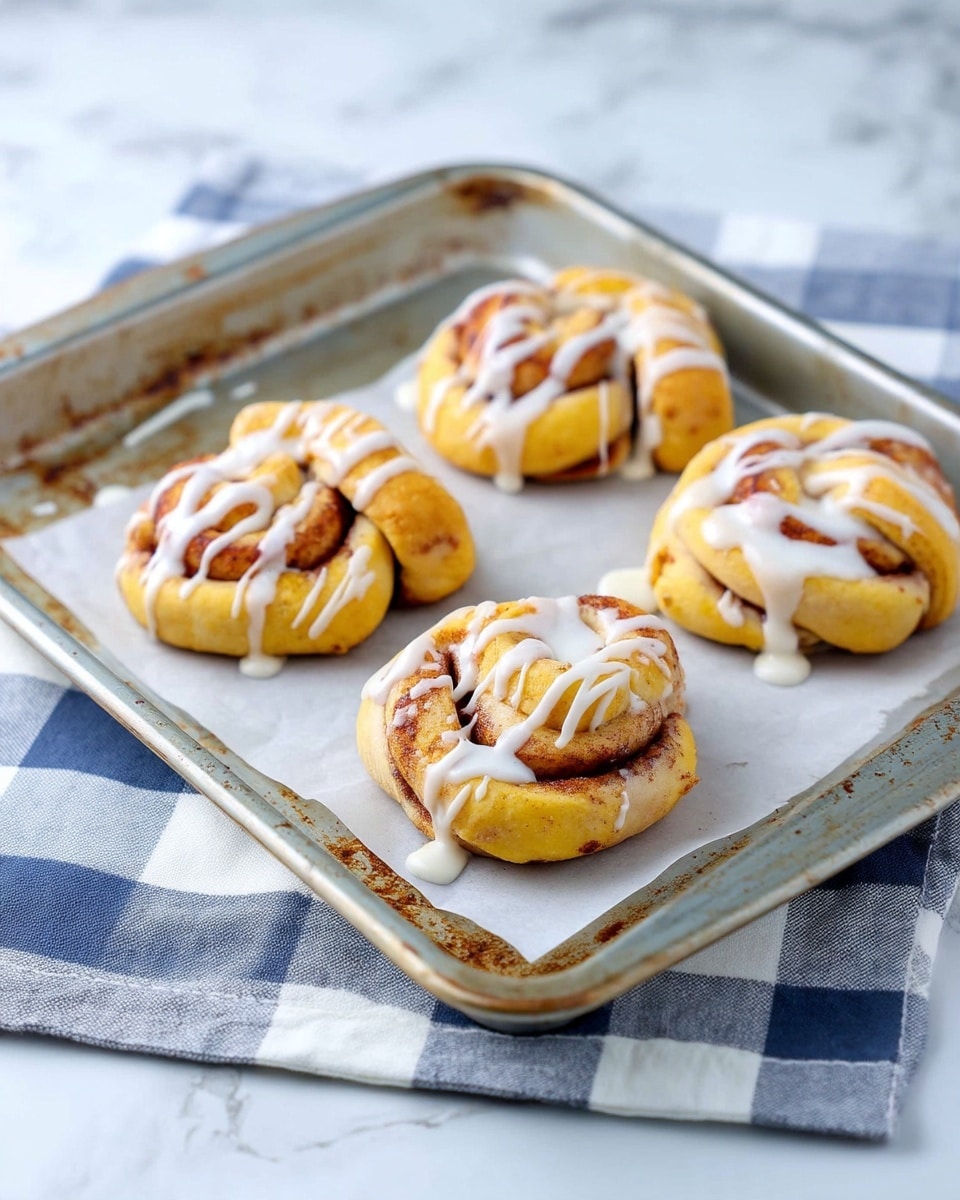 The image shows five small cinnamon rolls on a baking tray lined with parchment paper on top of a white and blue checkered cloth. Each roll has two visible layers: a soft, golden-brown dough layer twisted with a darker cinnamon sugar layer inside. White glaze with a smooth texture is drizzled unevenly over the tops, creating a glossy contrast on the rolls. The tray has slight discolorations and a metal rim, and the background is a white marbled texture. Photo taken with an iphone --ar 4:5 --v 7