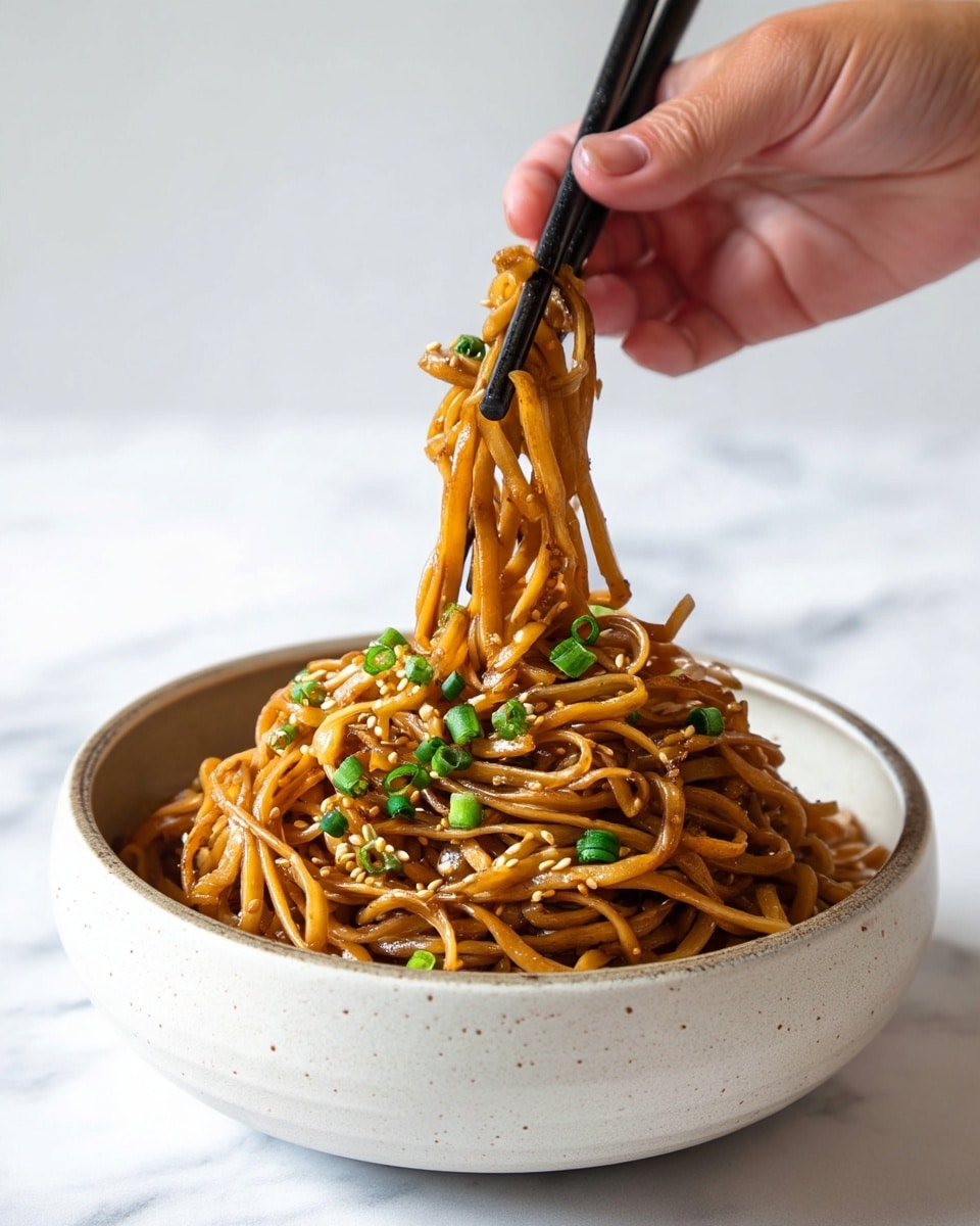 A speckled off-white bowl on a white marbled surface is filled with glossy light brown noodles coated in sauce. The noodles have a slight shine and are mixed with small pieces of green onions and sprinkled white sesame seeds, adding texture and pops of green and off-white color. A pair of black chopsticks, held by a woman's hand, is lifting a small bunch of noodles from the bowl. Photo taken with an iphone --ar 4:5 --v 7